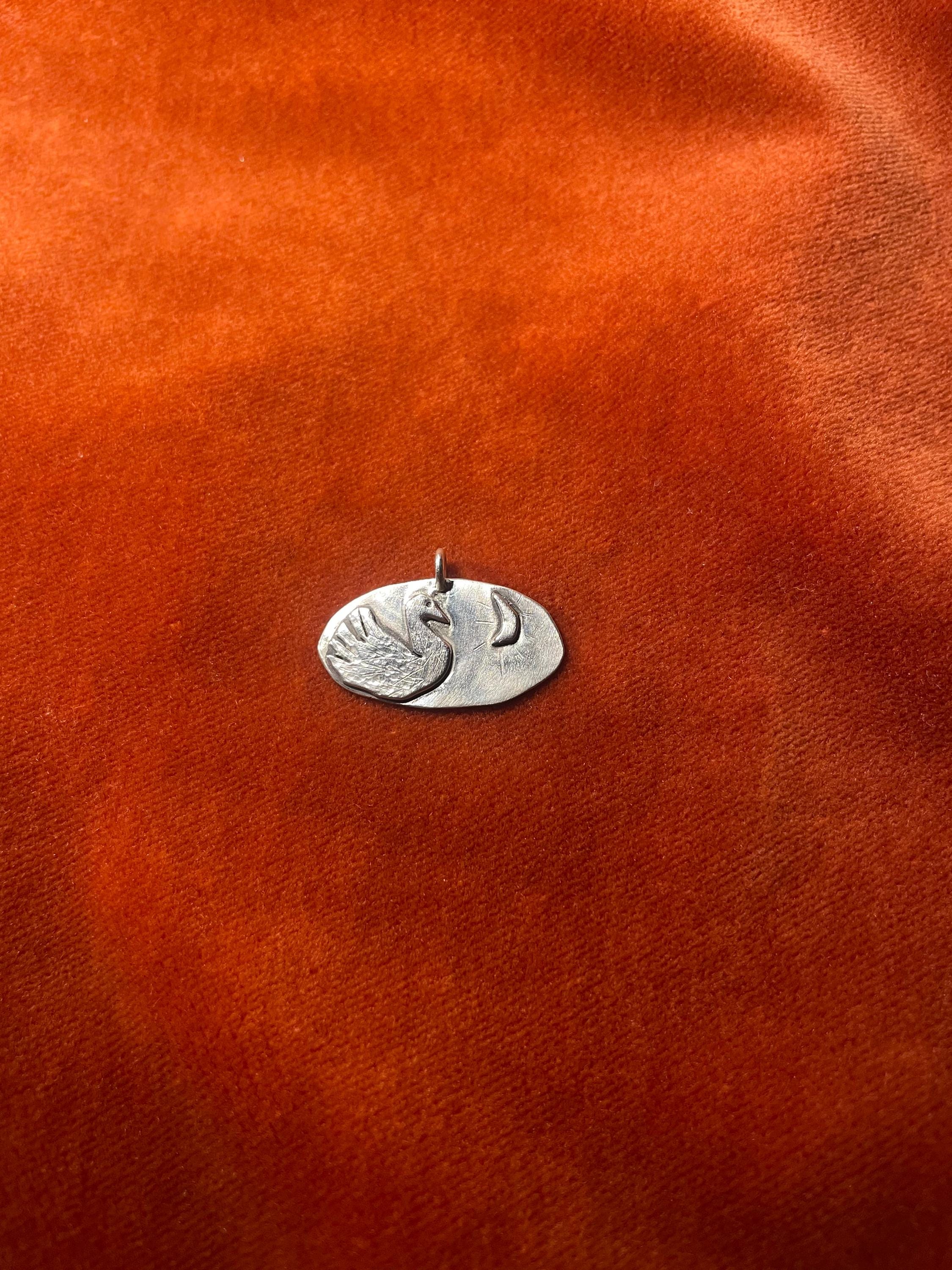 Silver swan charm on an orange velvet surface.