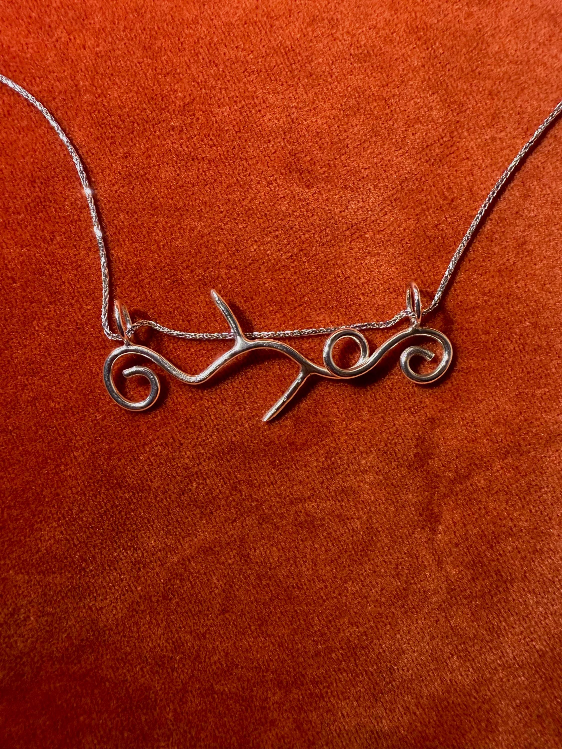 Silver vine shaped pendant on an orange background.