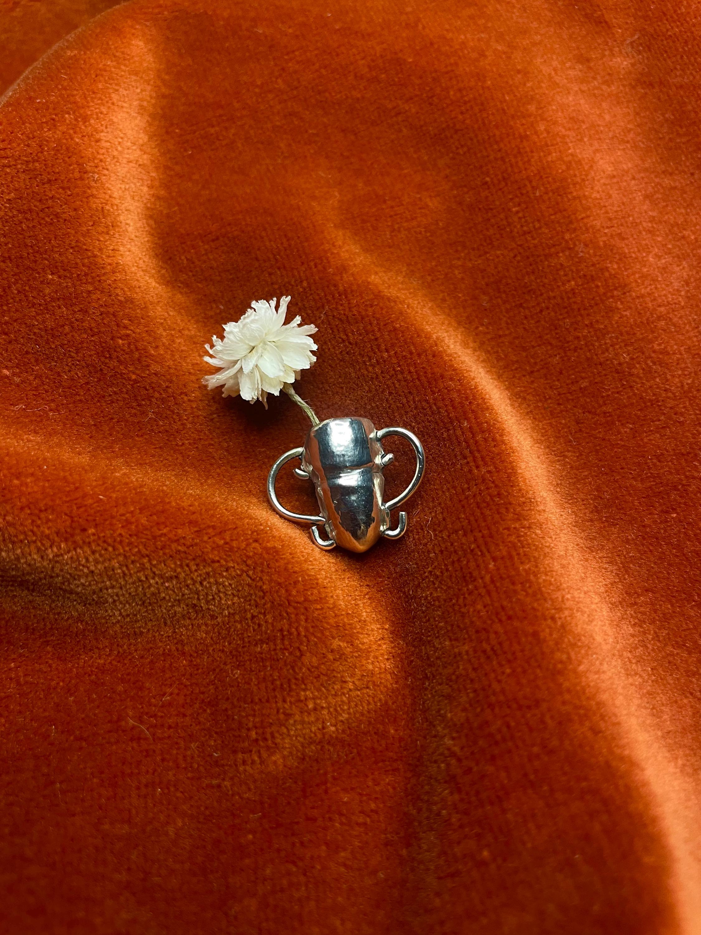 Silver vase with a white flower on an orange velvet background.
