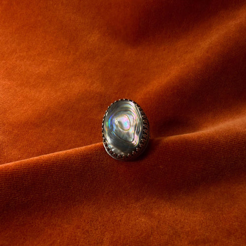 Silver ring with a colorful abalone oval shaped stone set in an ornate bezel sitting on a medium sized band.
