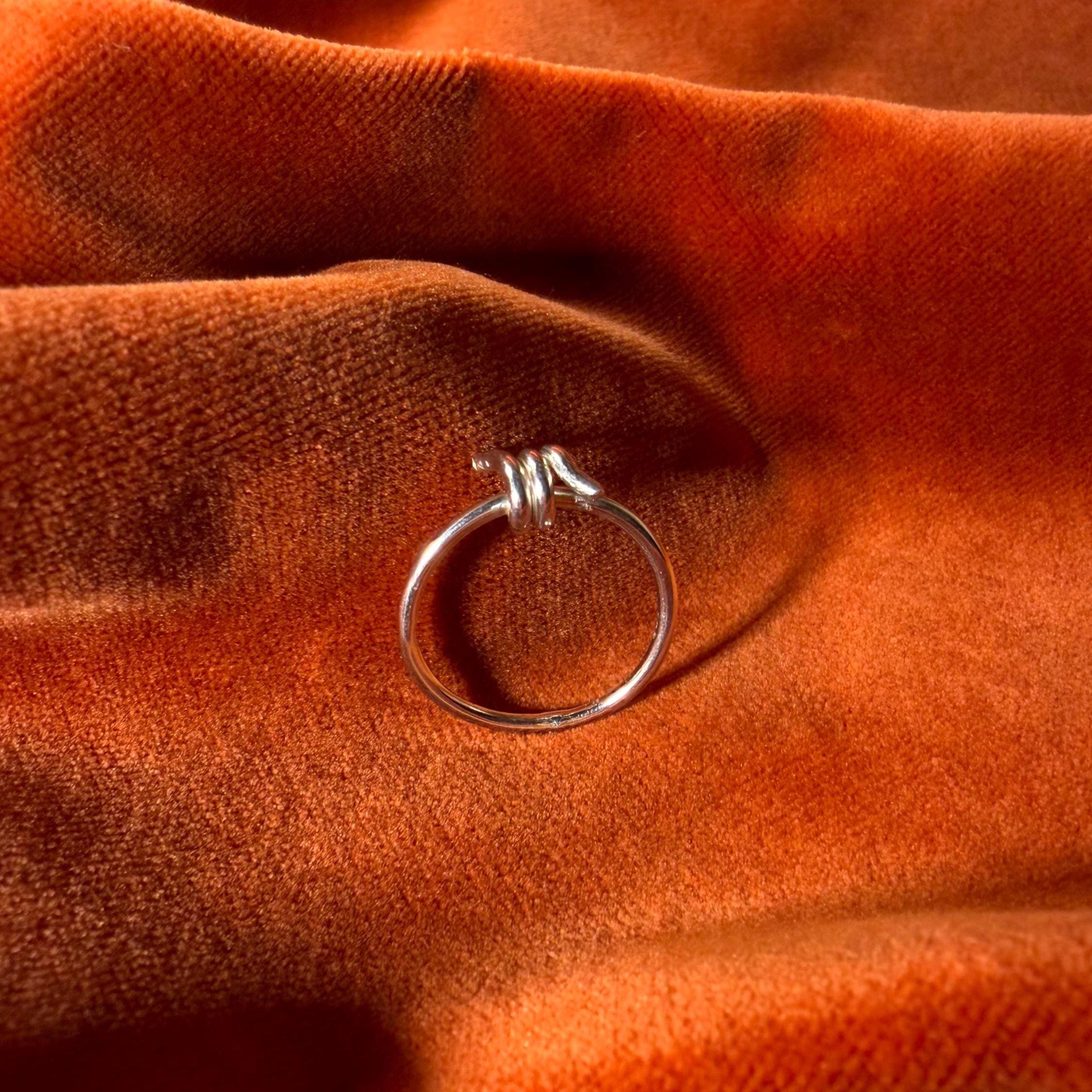 Silver ring with a design that features a barb on the top of the ring. Ring is staged on an orange velvet background.