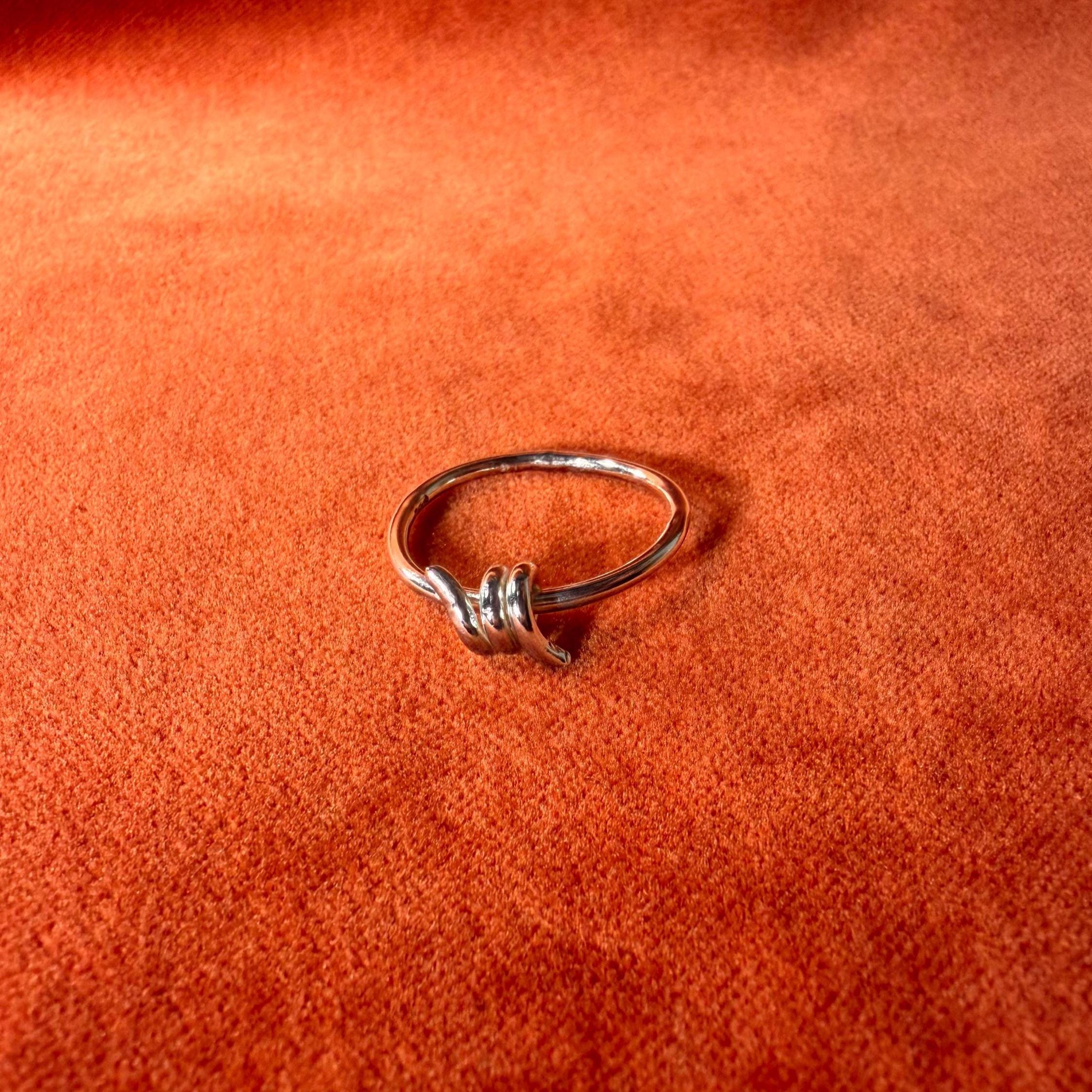 Silver ring with a design that features a barb on the top of the ring. Ring is staged on an orange velvet background.