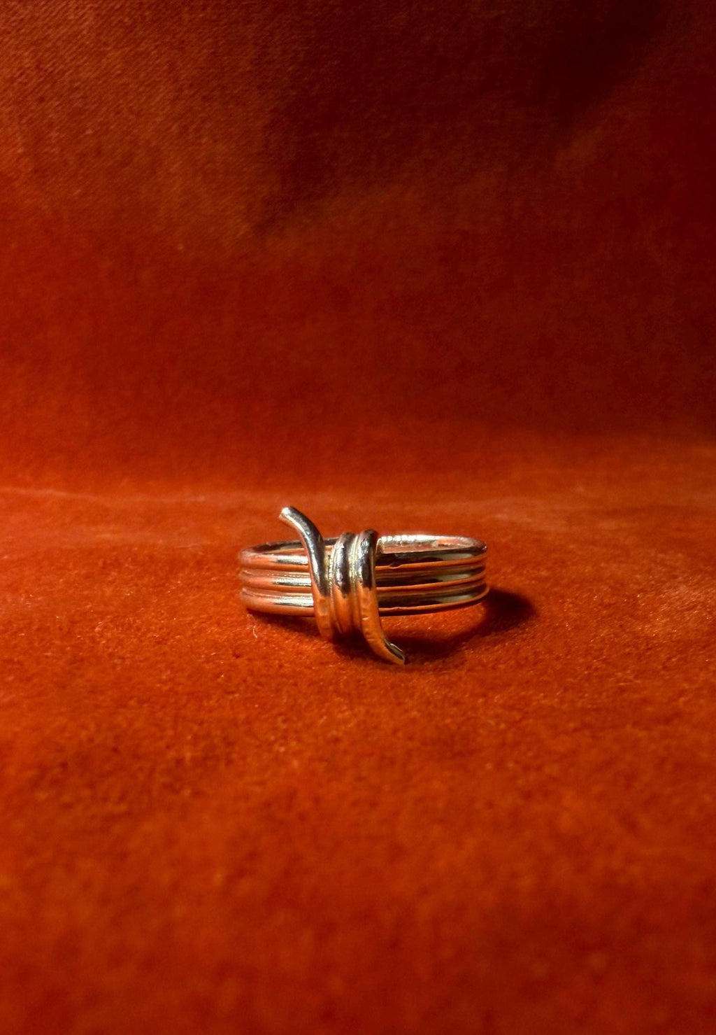 Silver ring featuring a barbed wire design. Staged on an orange velvet background.