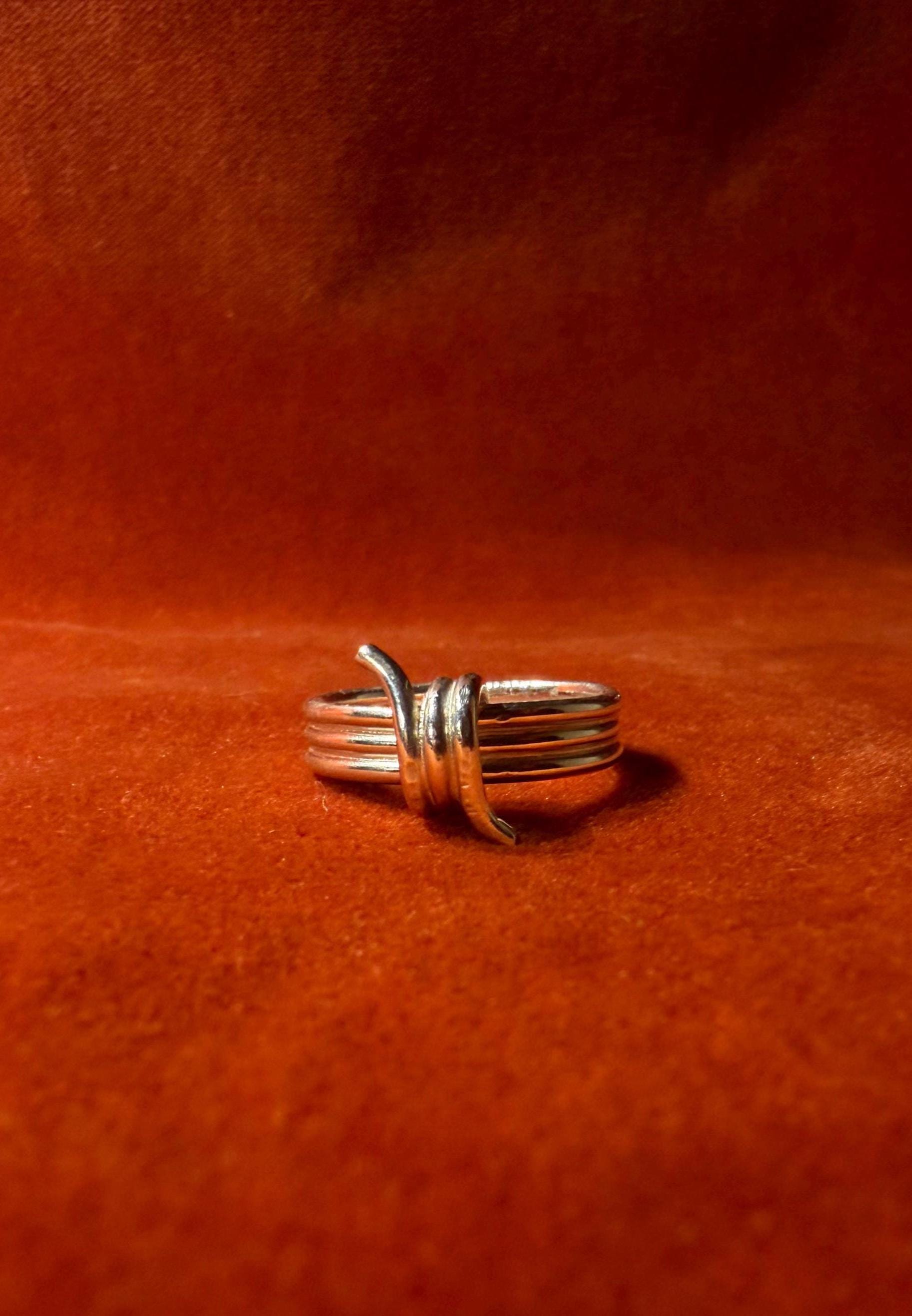 Silver ring featuring a barbed wire design. Staged on an orange velvet background.