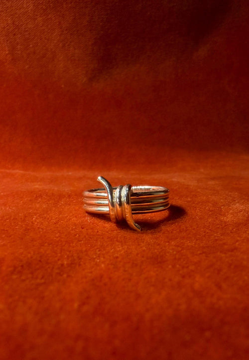 Silver ring featuring a barbed wire design. Staged on an orange velvet background.
