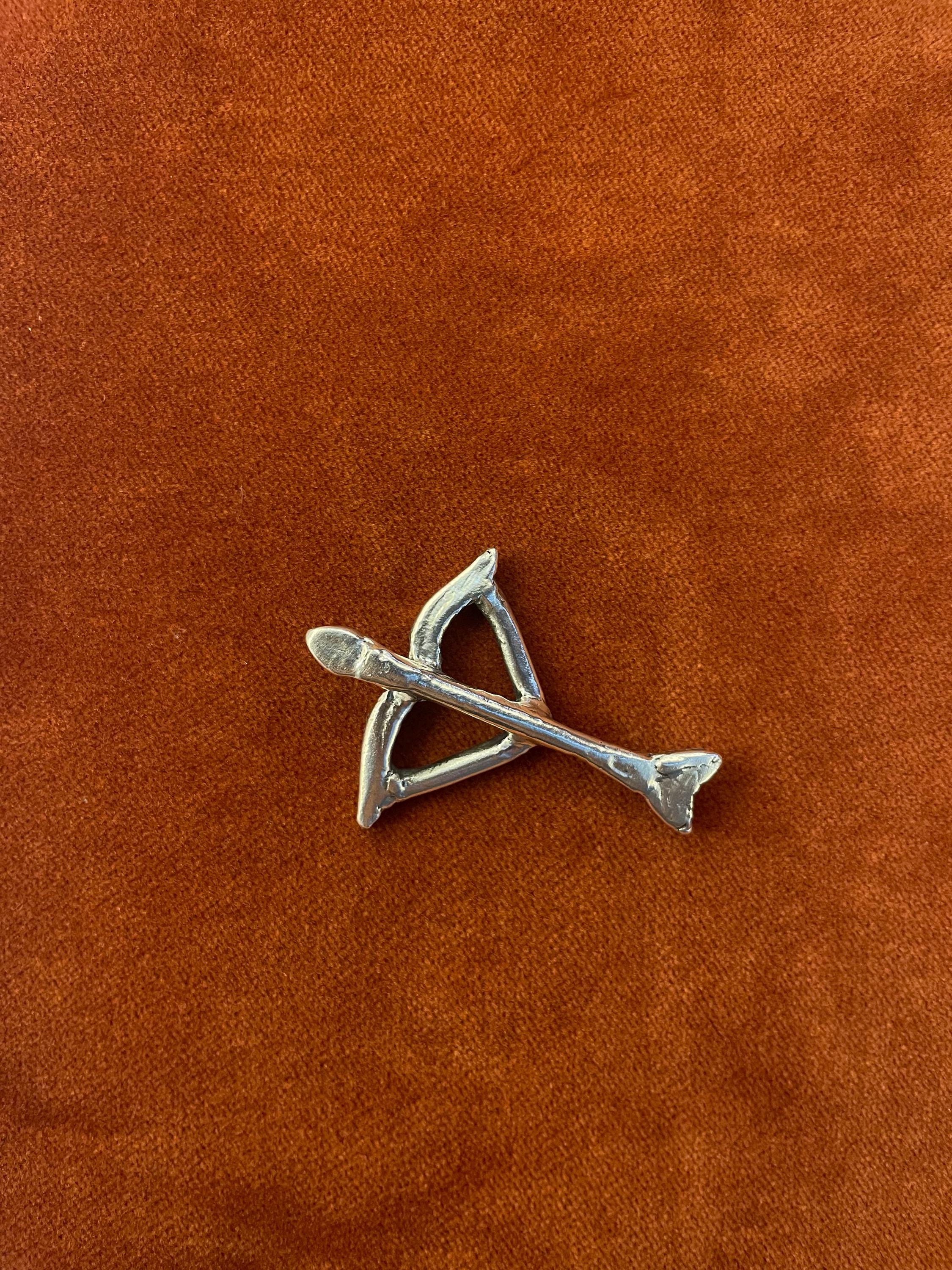 Silver bow and arrow charm. Laying against an orange velvet background.