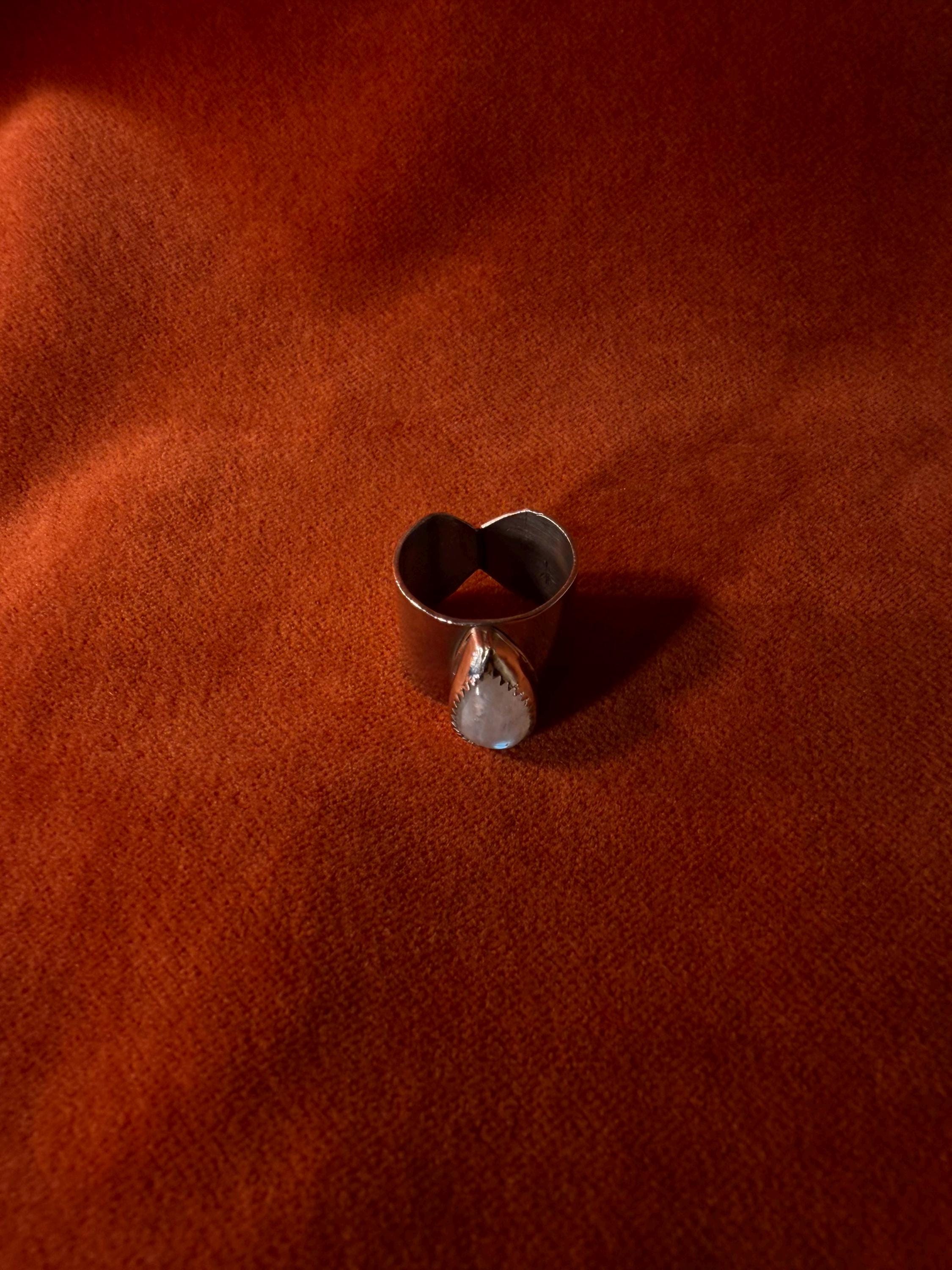 Silver ring with a teardrop shaped moonstone set on top of a chunky band against an orange velvet background.