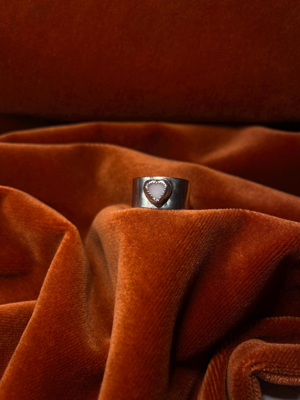 Silver ring with a pink opal stone set on a chunky band. Staged on an orange velvet backdrop.