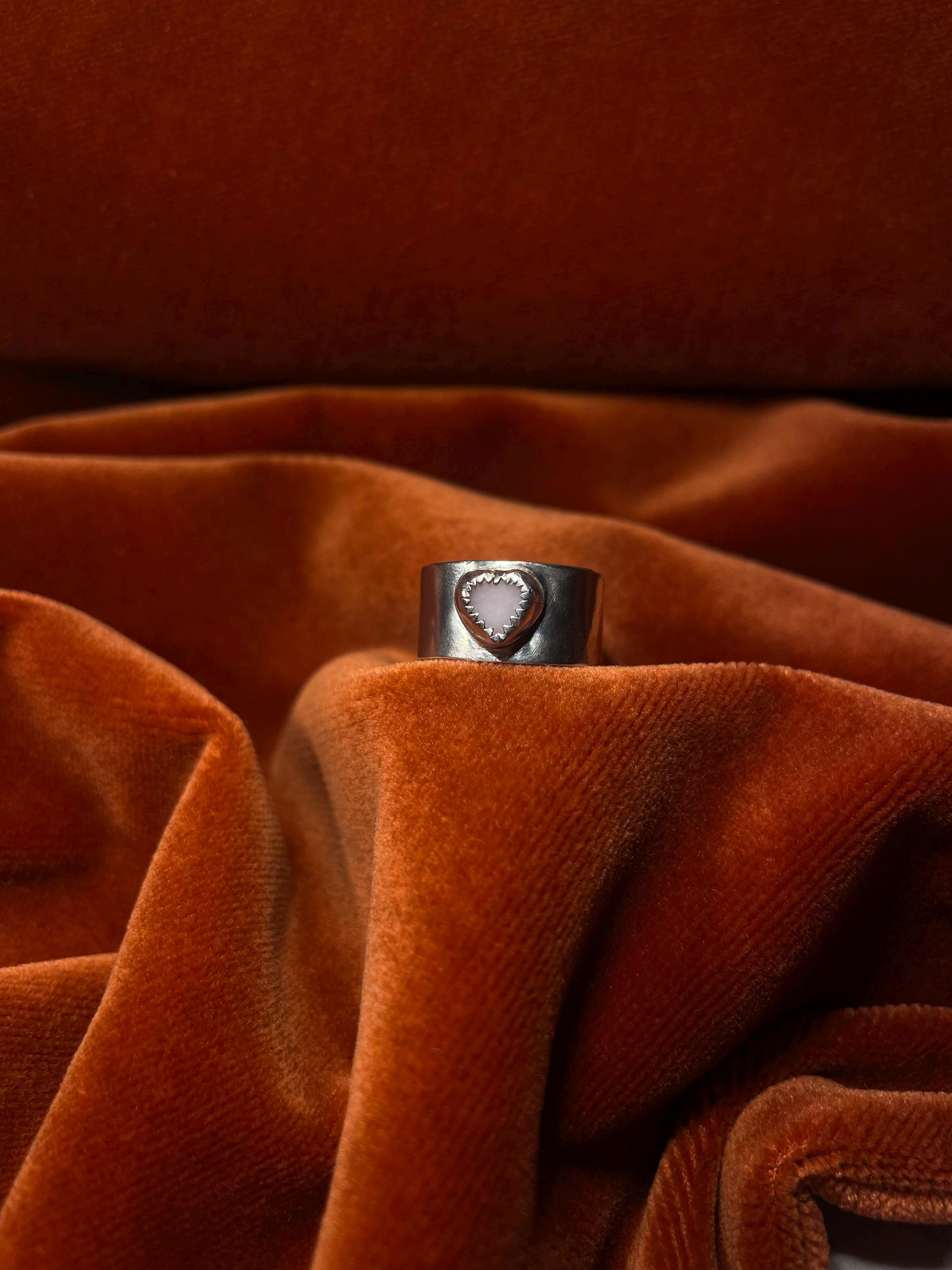 Silver ring with a pink opal stone set on a chunky band. Staged on an orange velvet backdrop.