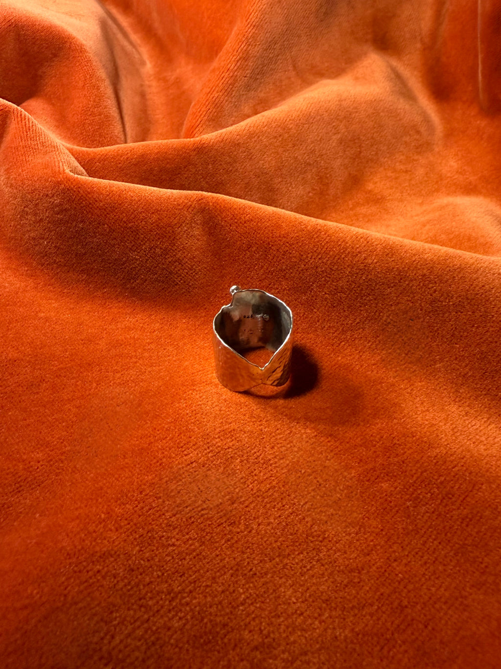 Close up image of the backside of asilver ring with a chunky hammered texture band. Staged on a orange velvet background.