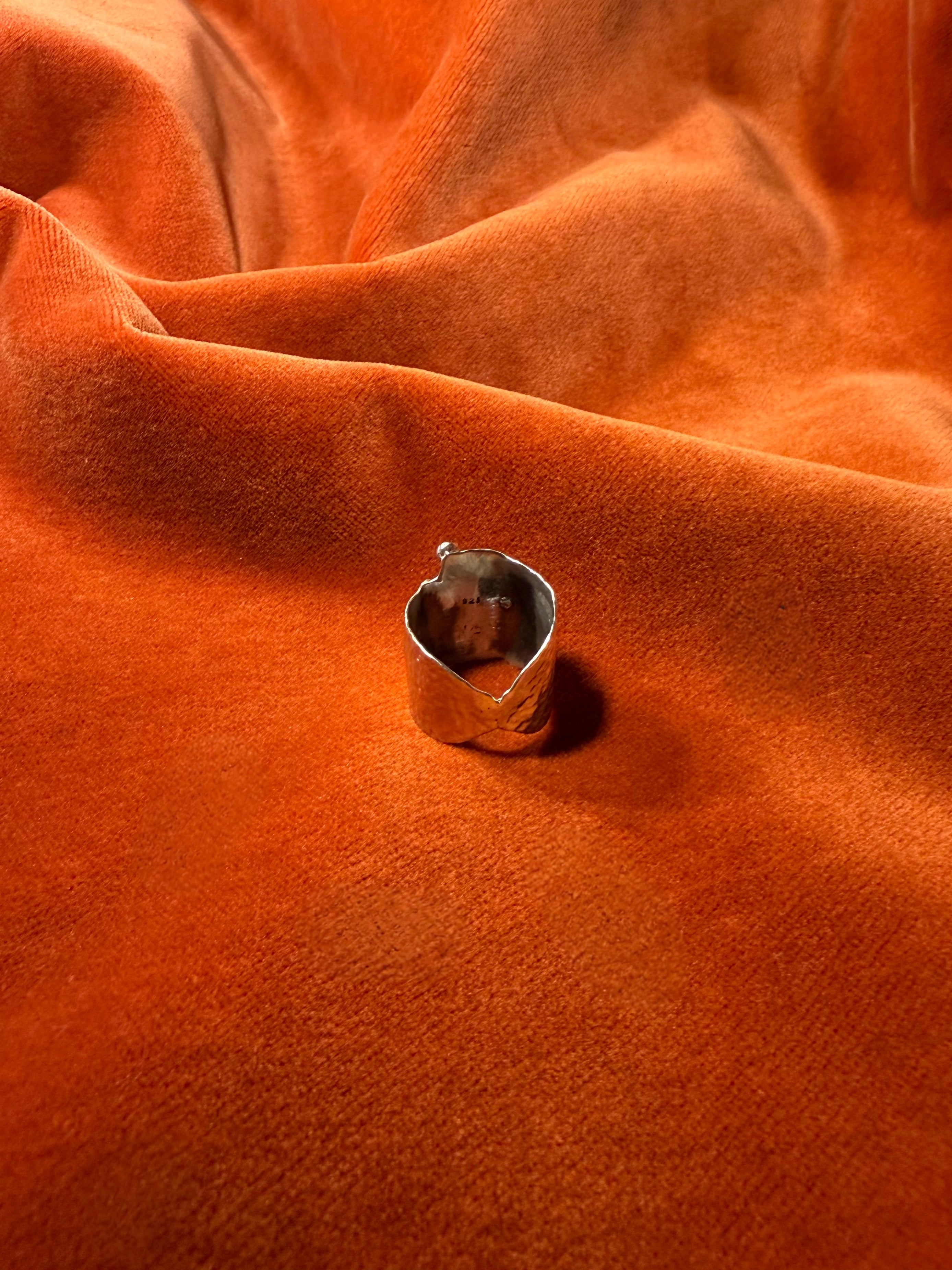 Close up image of the backside of asilver ring with a chunky hammered texture band. Staged on a orange velvet background.