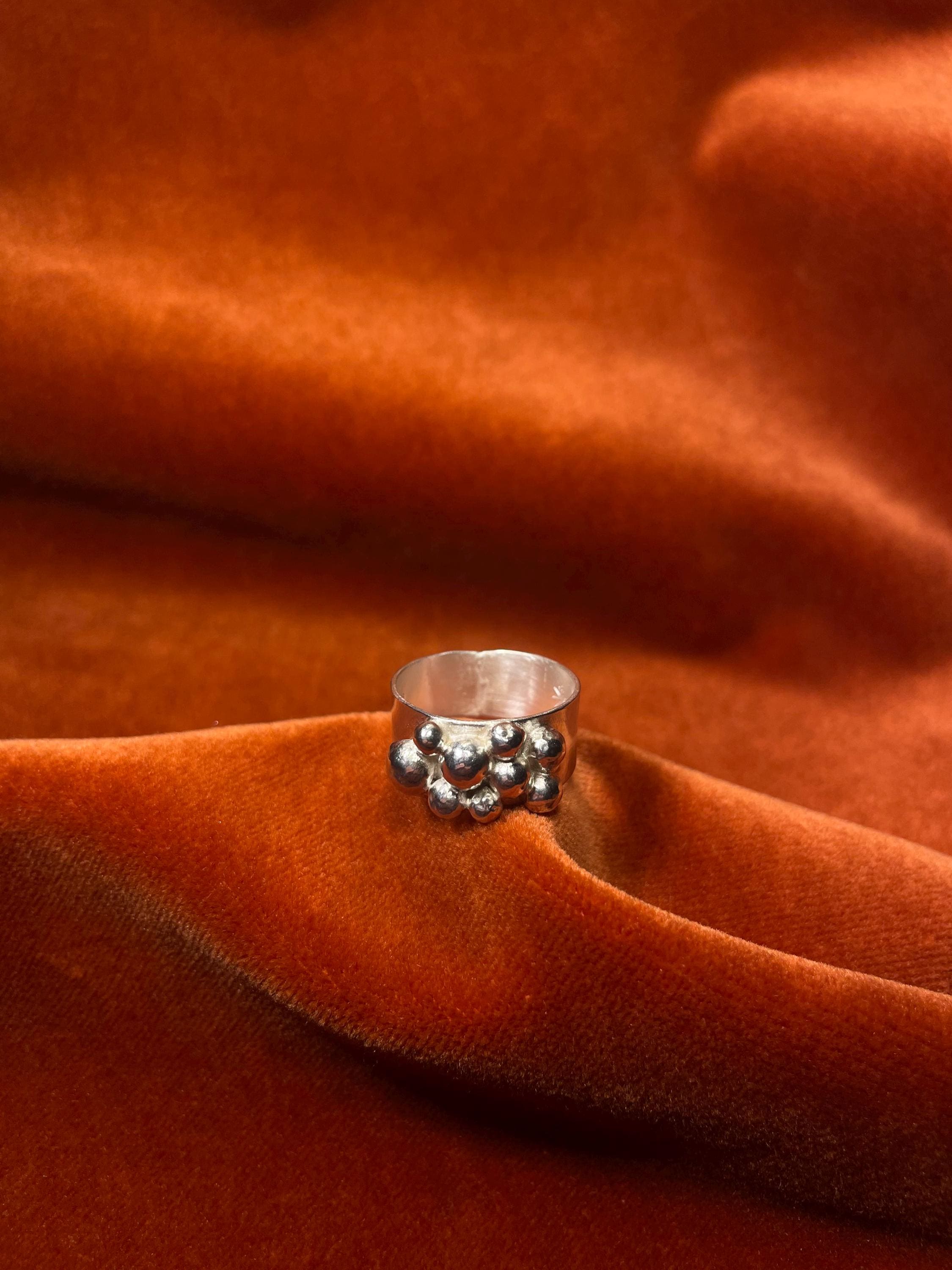Silver ring with bubbles forming around the band laying on an orange velvet backdrop.