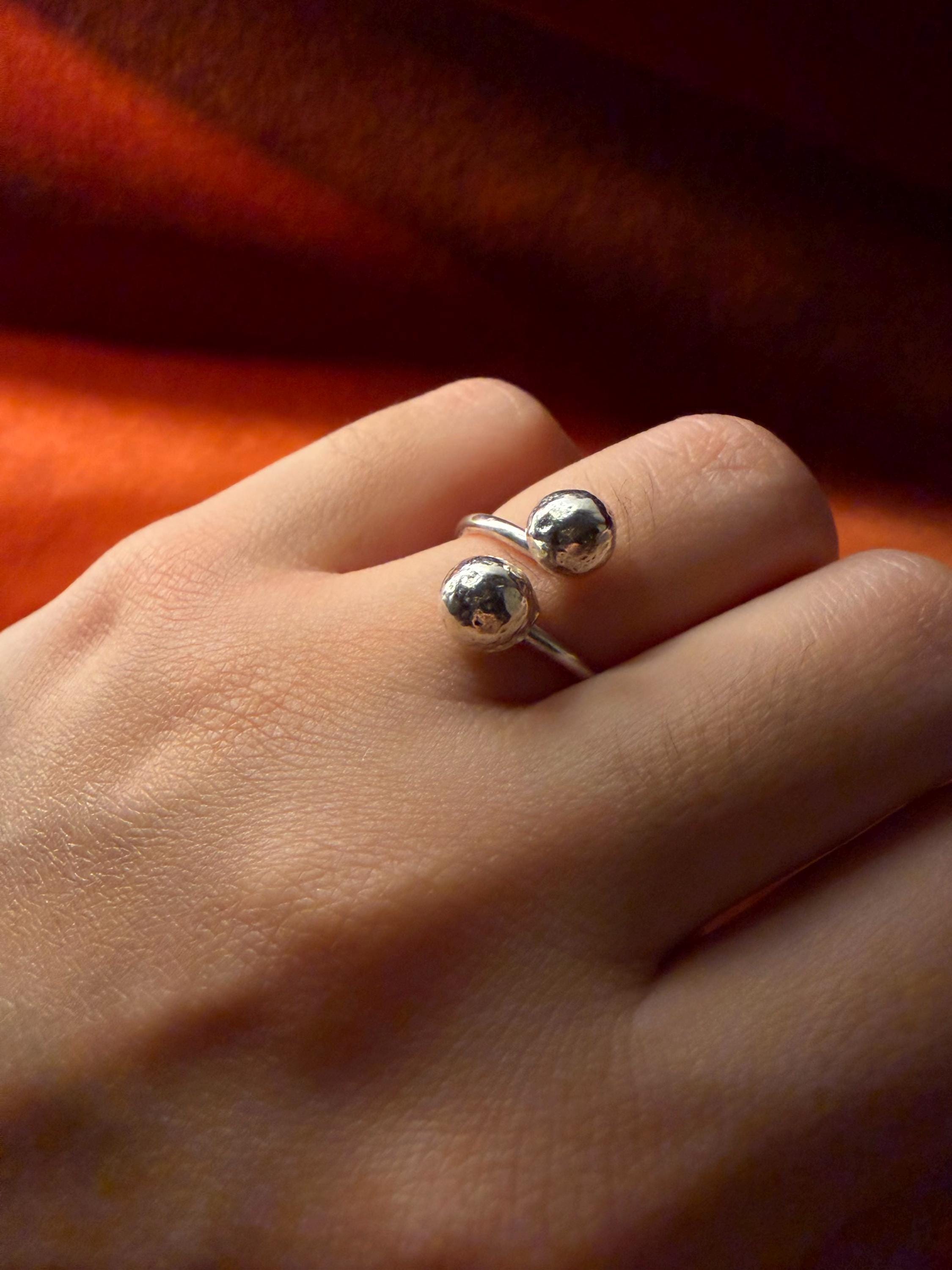 Model's hand wearing a silver ring with two orbs designed at each end of the ring. 
