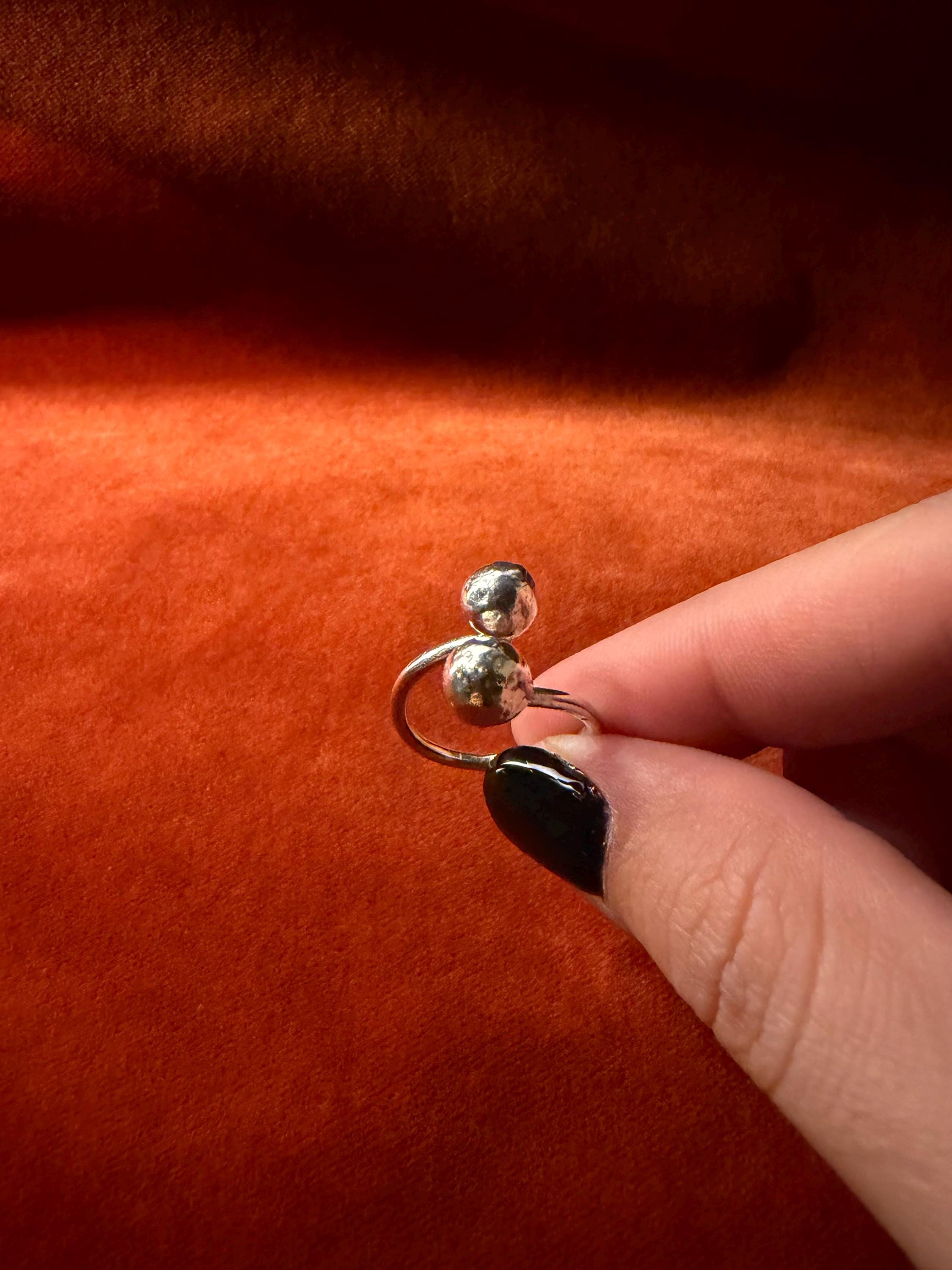 Model's hand holding a silver ring with two orbs designed at each end of the ring. 