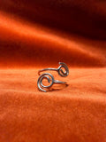 Silver ring with spirals on each end of the ring. The is staged against an orange velvet backdrop. 