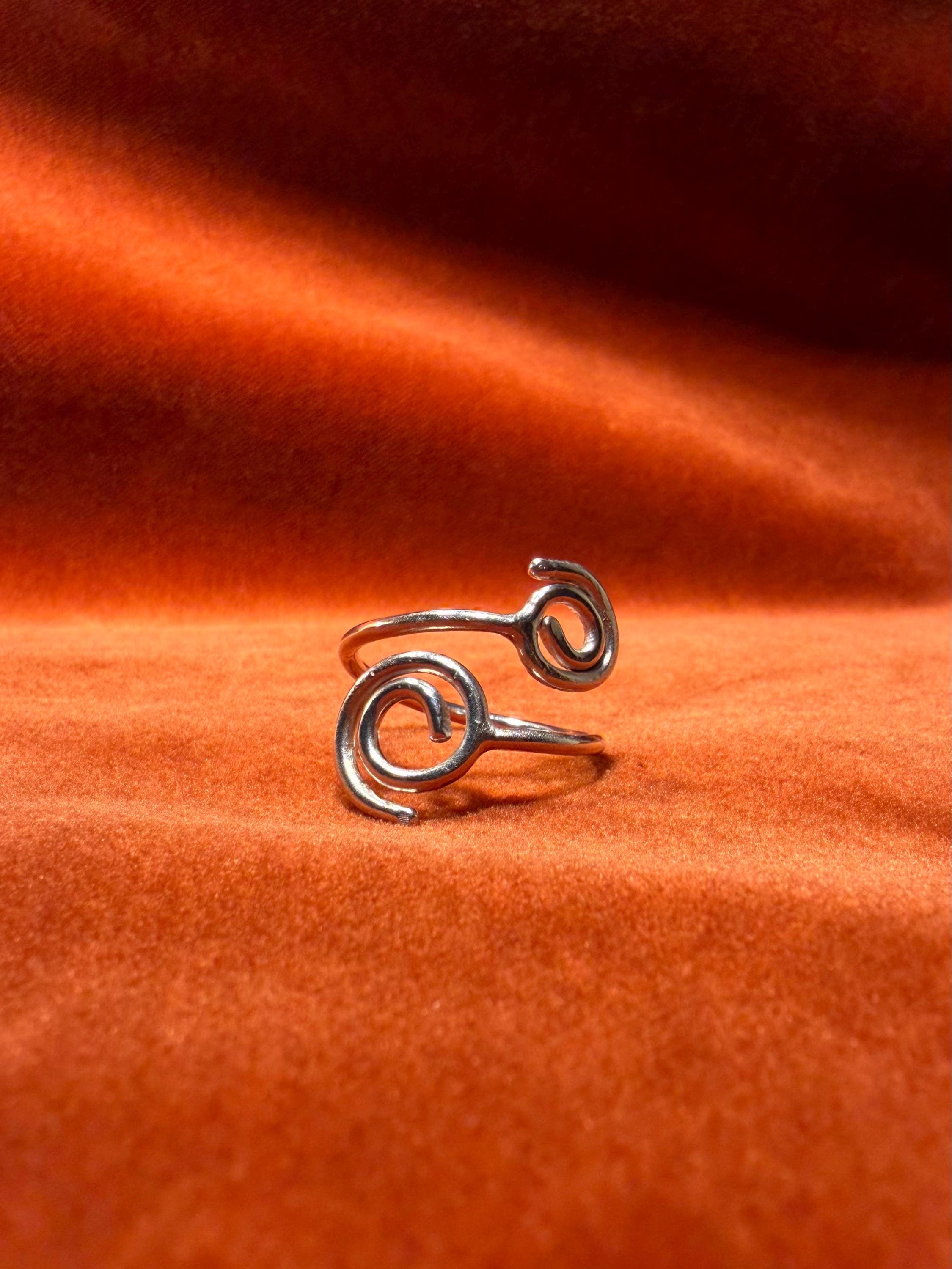 Silver ring with spirals on each end of the ring. The is staged against an orange velvet backdrop. 