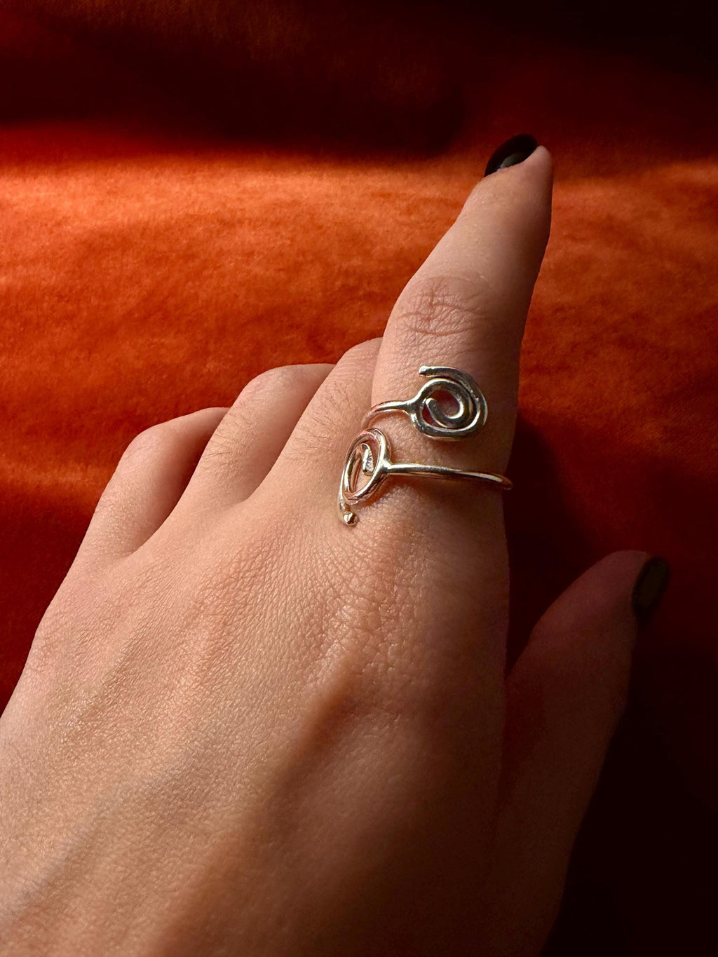Model's hand wearing a silver ring on the index finger. The ring features two spirals at each end, overlapping the other. 
