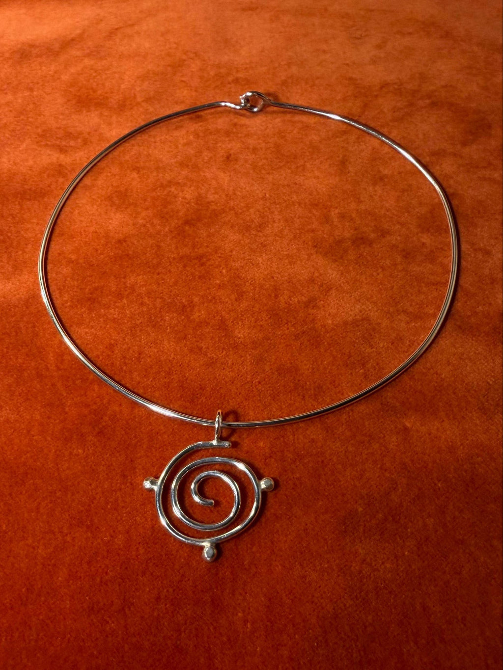 Silver spiral pendant with three orbs surrounding the edge of the charm. The pendant is looped necklace on an orange background
