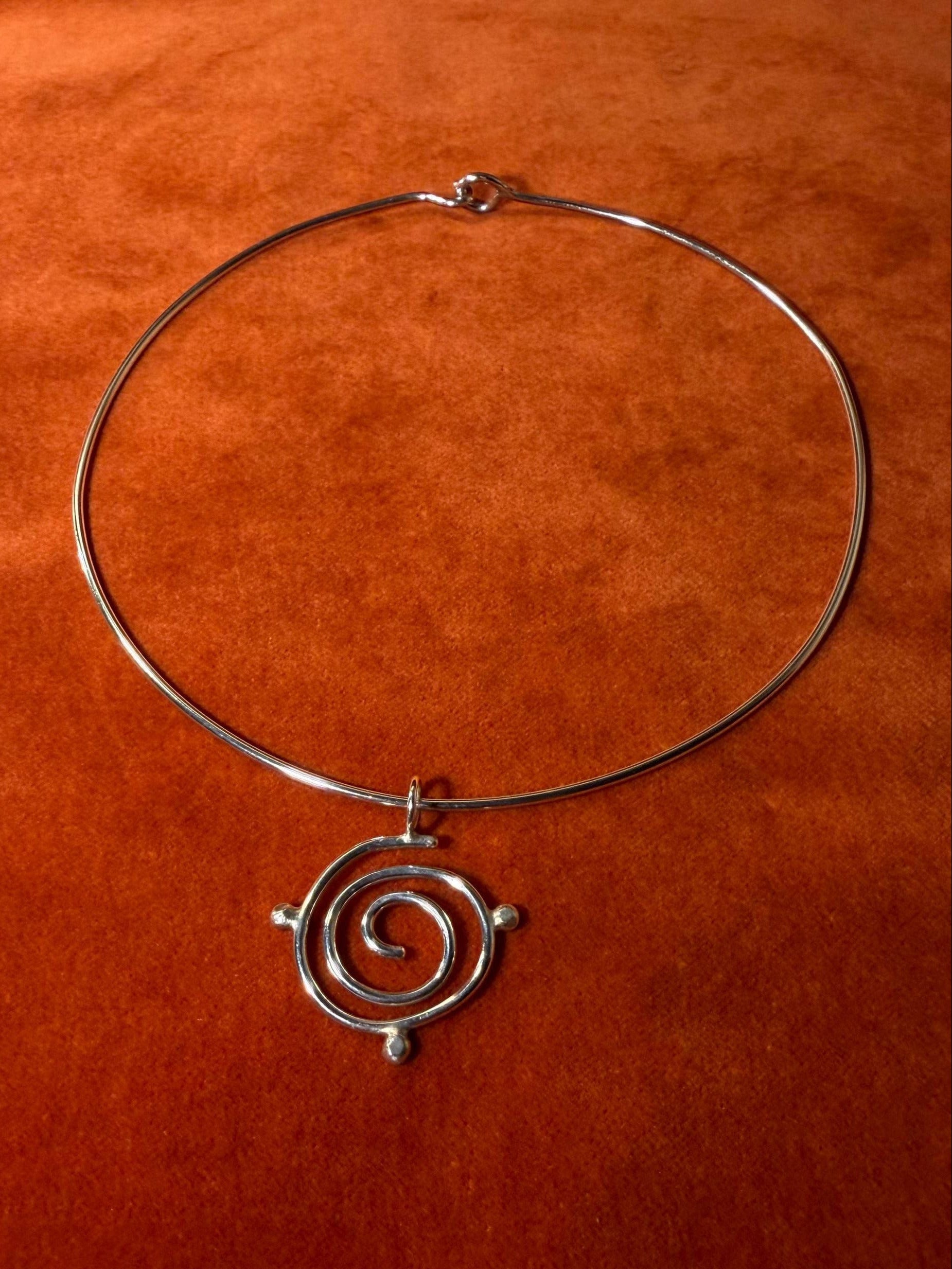 Silver spiral pendant with three orbs surrounding the edge of the charm. The pendant is looped necklace on an orange background