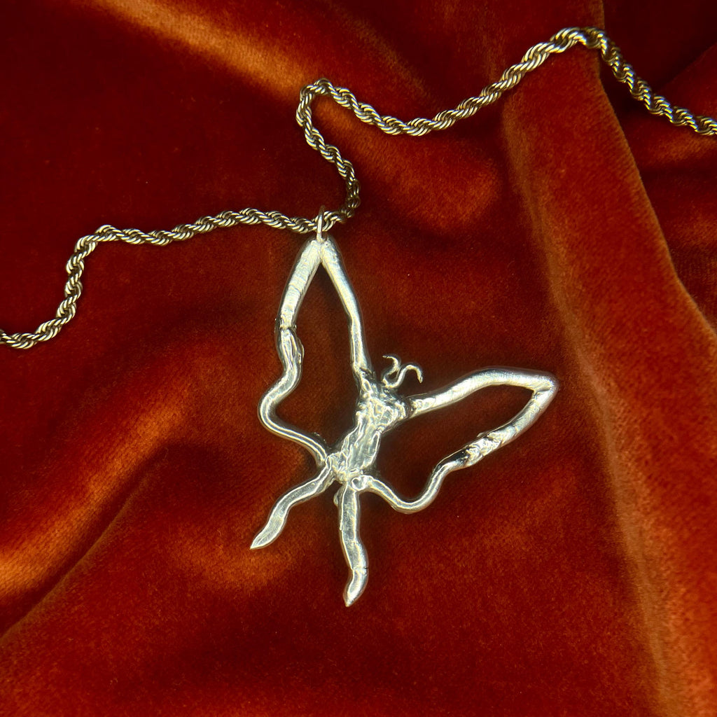 Butterfly-shaped pendant on a chain against a red fabric background