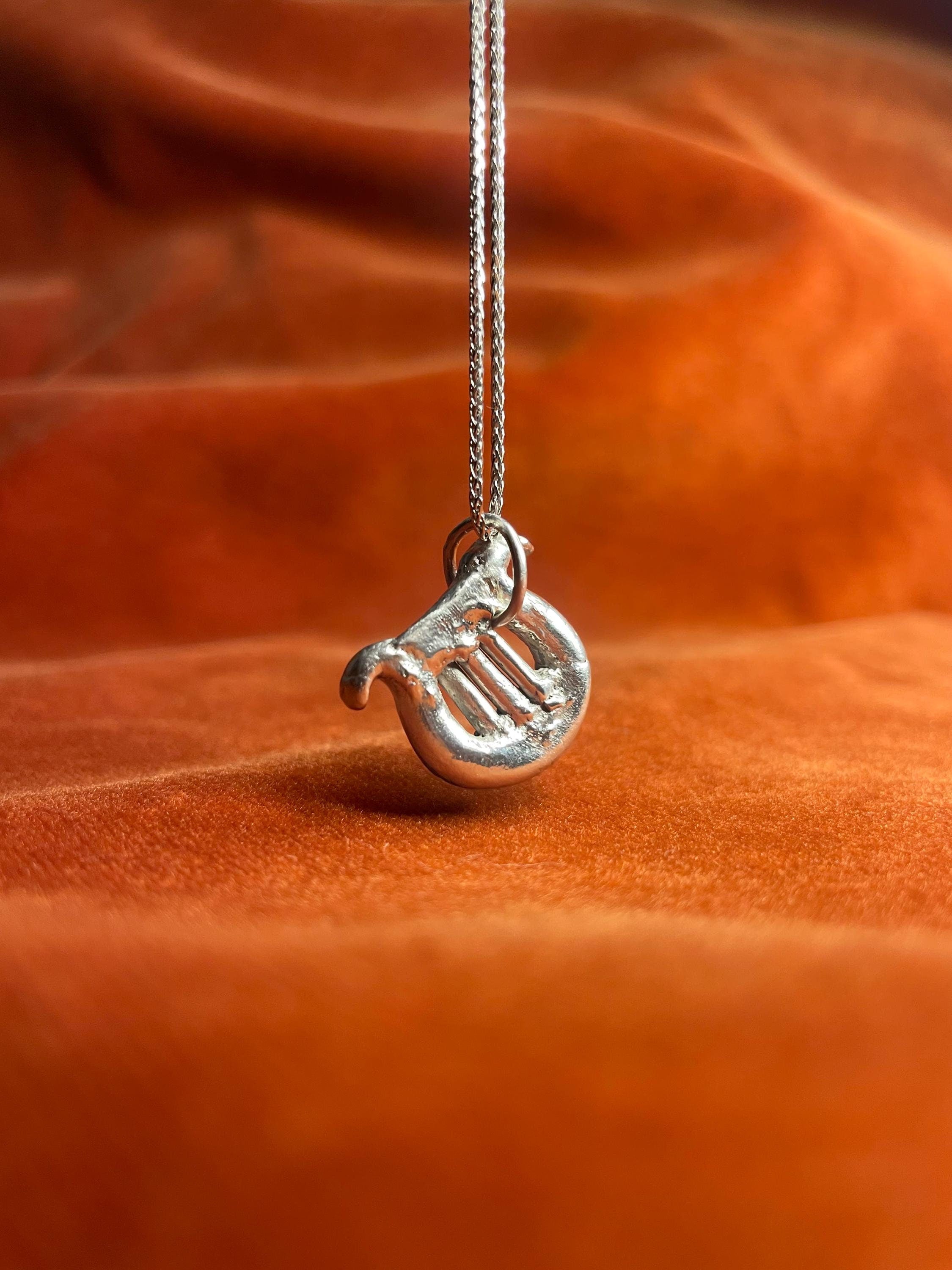 Silver harp with a silver jump ring dangling on a silver chain. Staged against an orange velvet background.