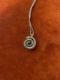 Silver spiral charm on a silver chain laying on an orange velvet background.
