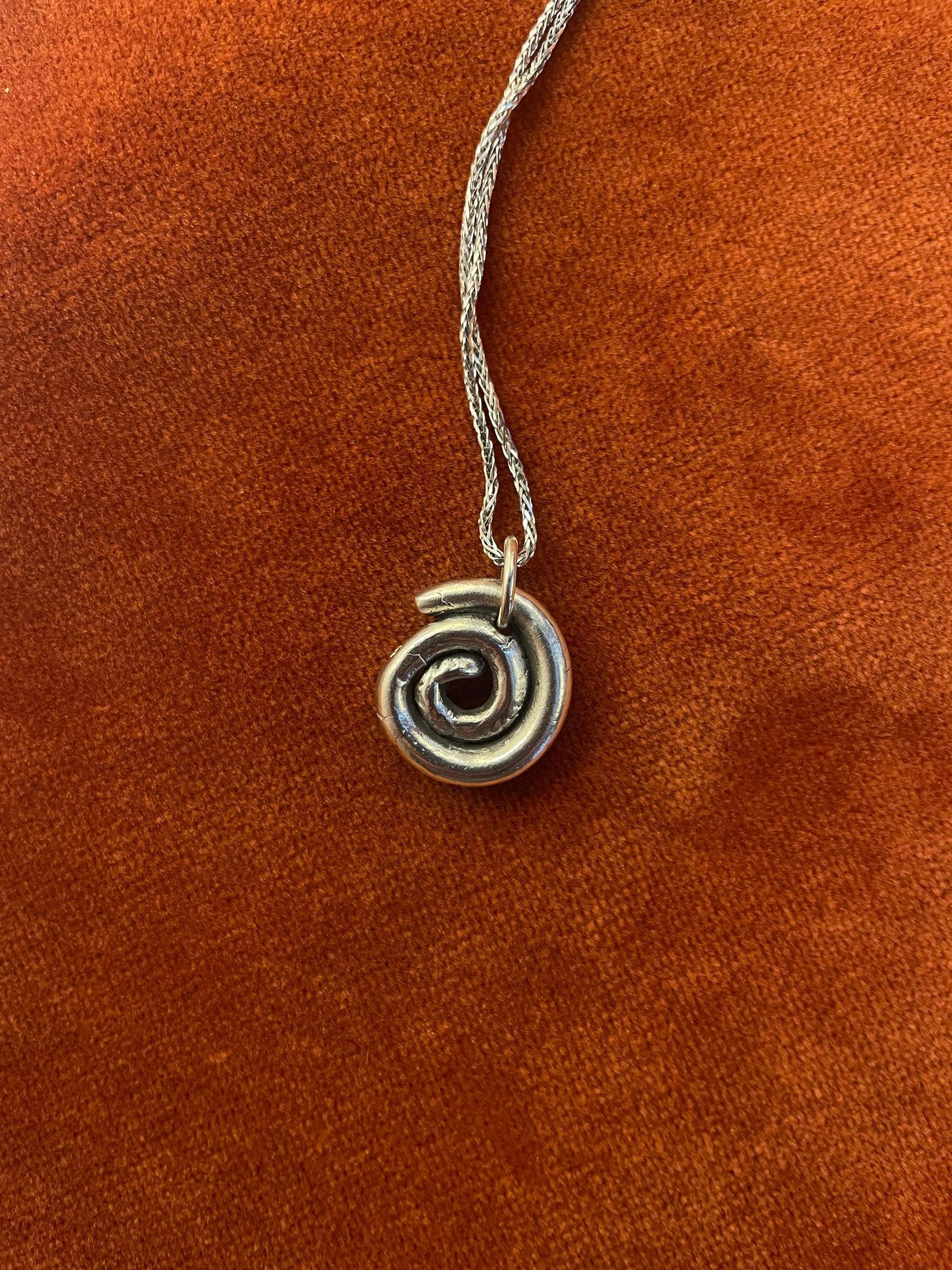 Silver spiral charm on a silver chain laying on an orange velvet background.