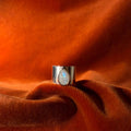 Silver ring with a teardrop shaped moonstone set on top of a chunky band against an orange velvet background.