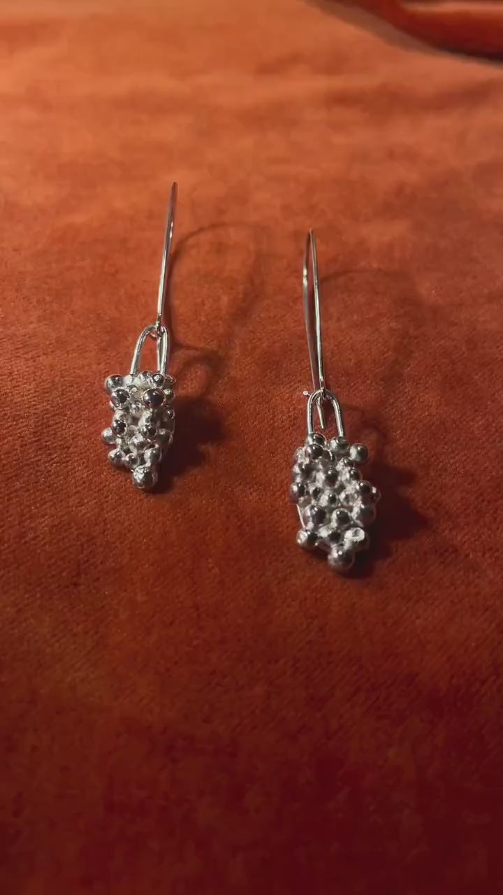 Video of a model's hand picking up a pair of silver earrings with clusters of bubbles with an elongated clasp hook for a dangling style.