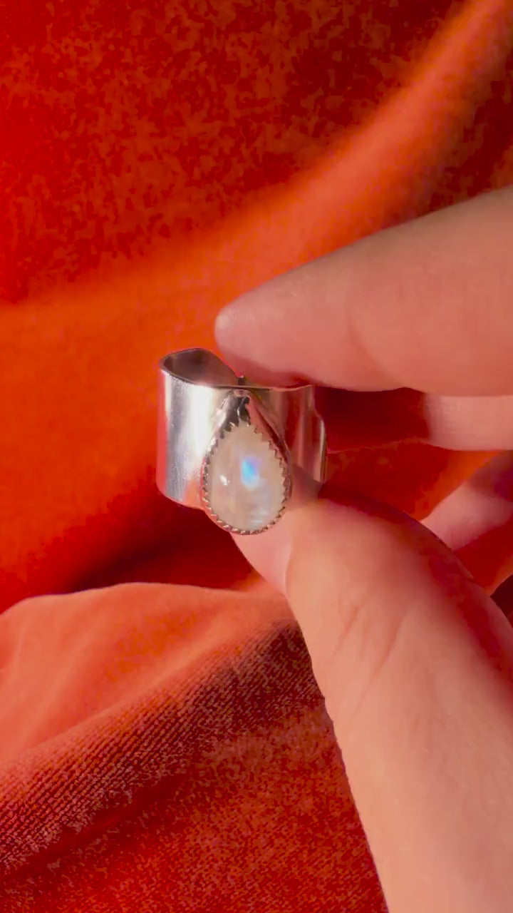 Silver ring with a teardrop shaped moonstone set on top of a chunky band against an orange velvet background.