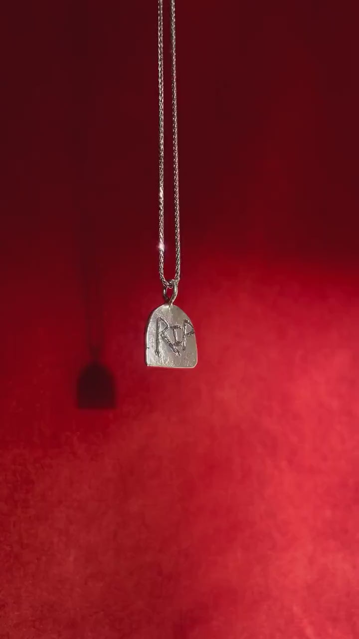 Video of a silver headstone charm with the letters RIP etched into it. Charm dangles from a silver necklace.