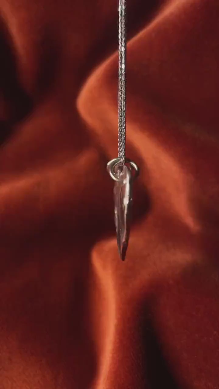 Silver heart shaped charm on a silver necklace over an orange velvet background.