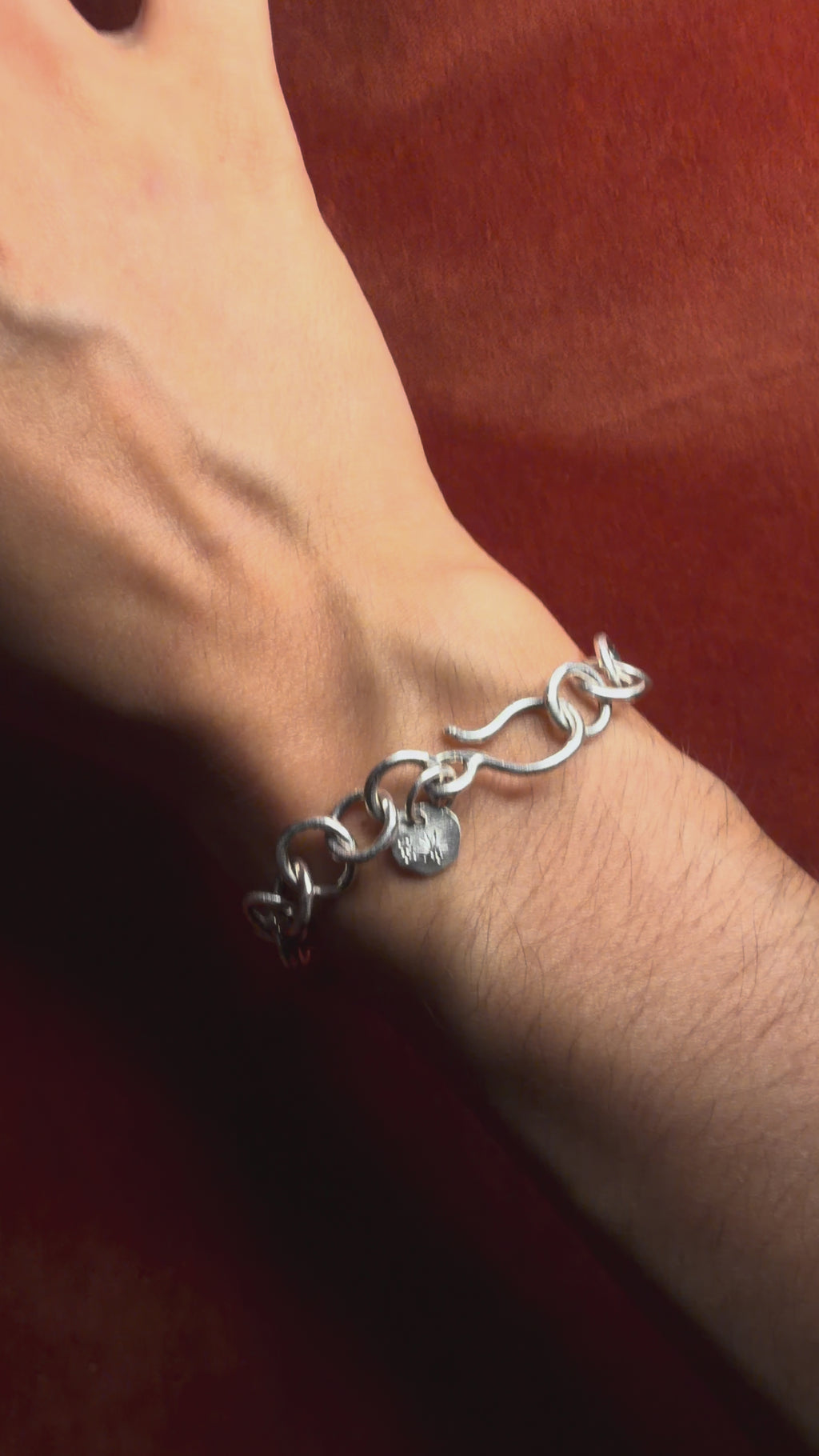 Video of a model showing a sterling silver chunky chain on their wrist. Displayed on an orange velvet backdrop.