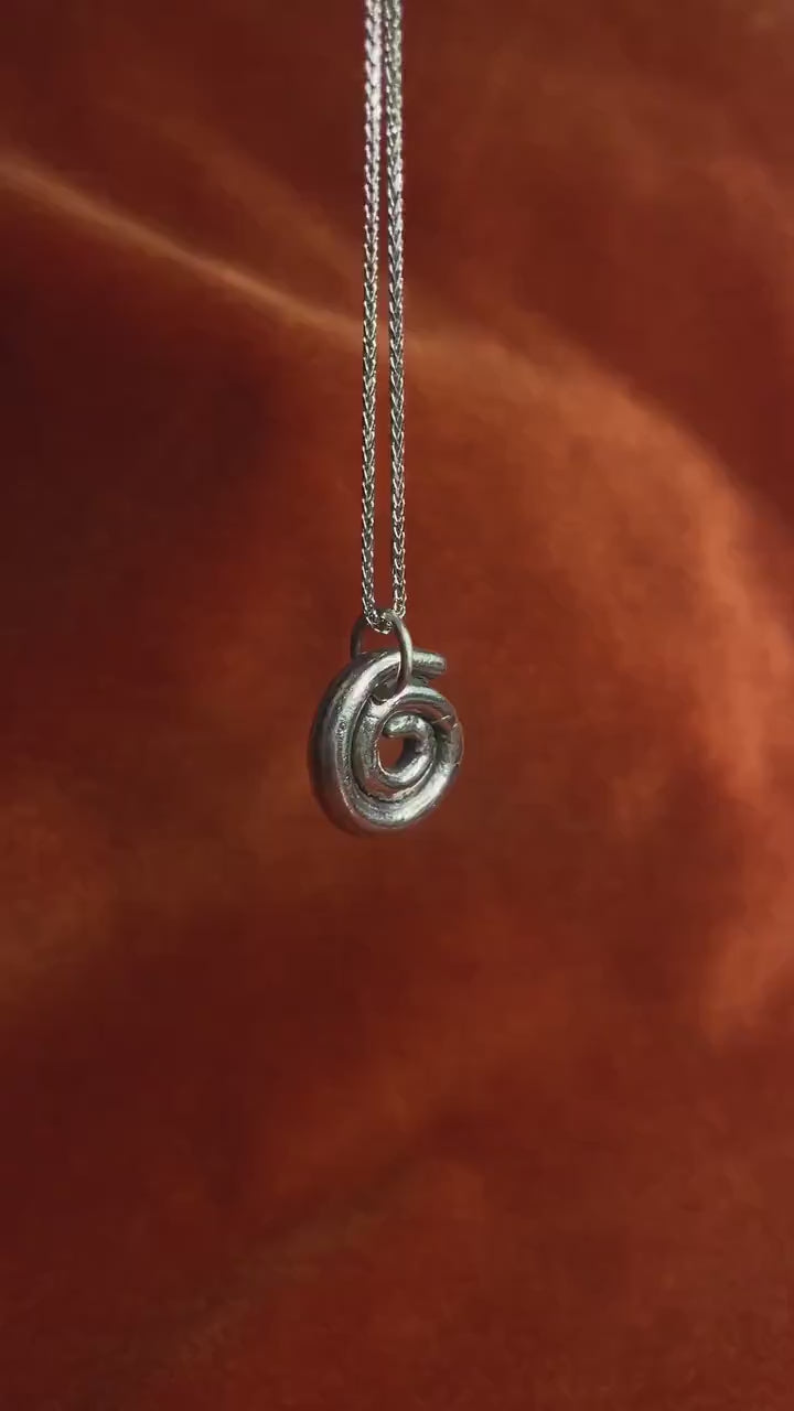 Silver spiral charm on a silver chain necklace dangling over an orange background.