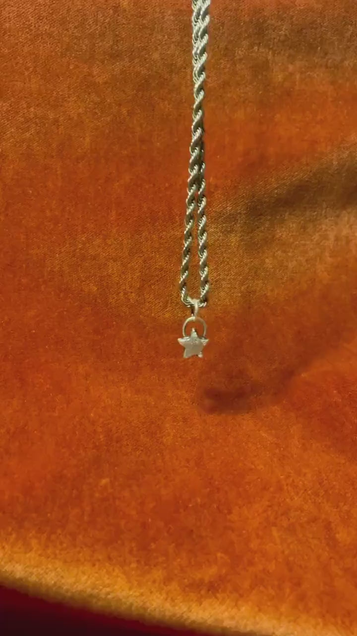 Video of a tiny star shape charm on a silver necklace in front of an orange background.