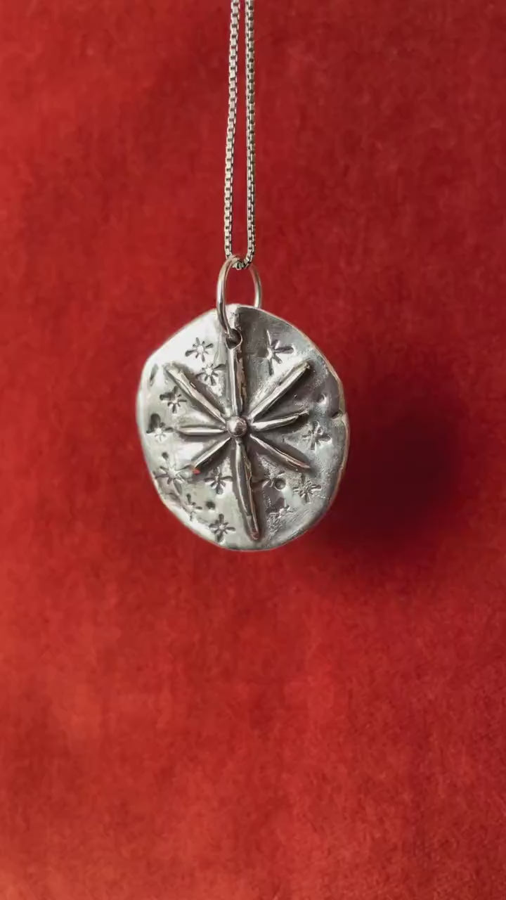 Video of silver starburst celestial charm dangling on a silver necklace.
