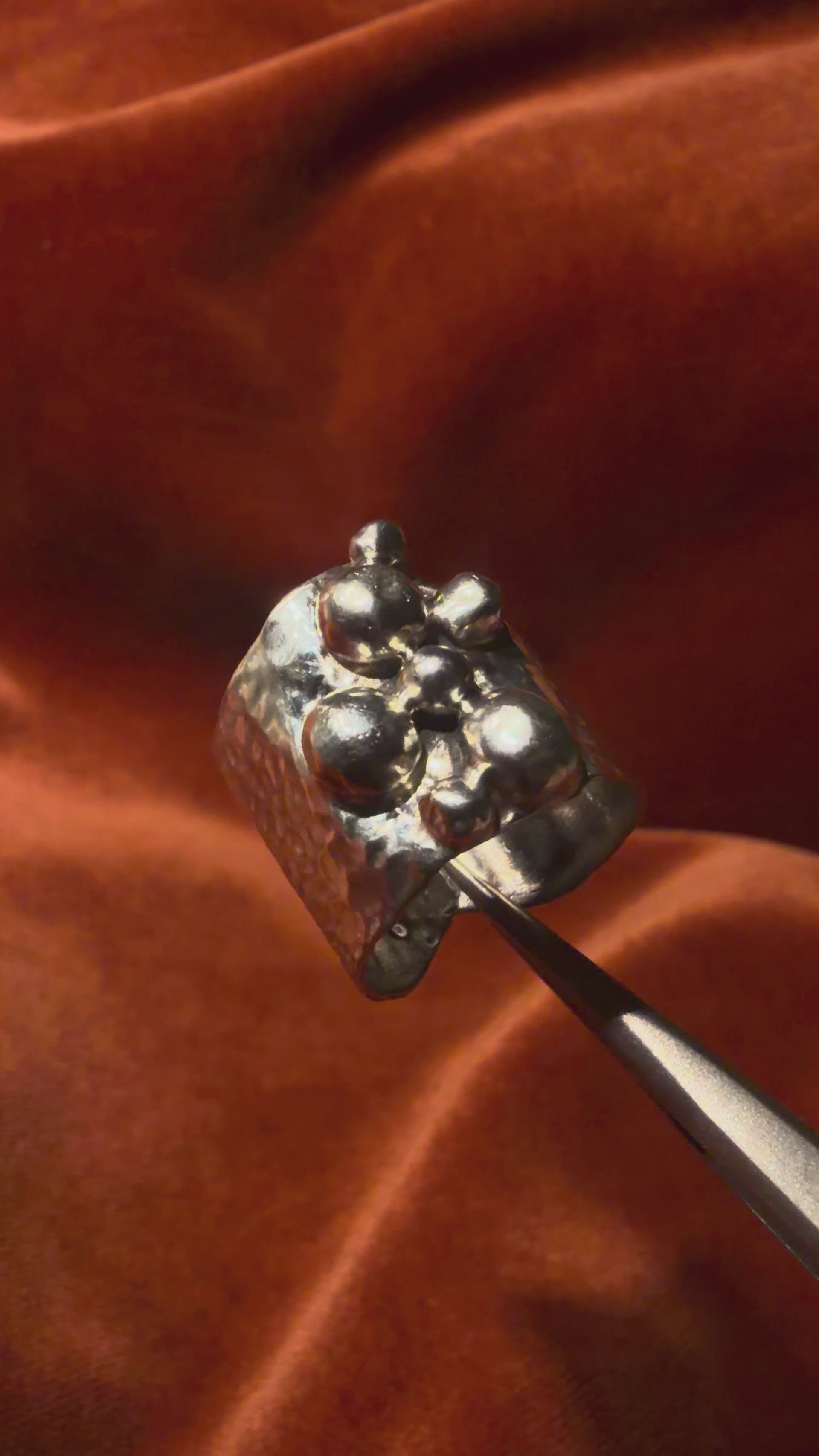 Video of a silver ring with a chunky hammered texture band. Seven varying sizes of orbs sit asymmetrically on top of the band. 