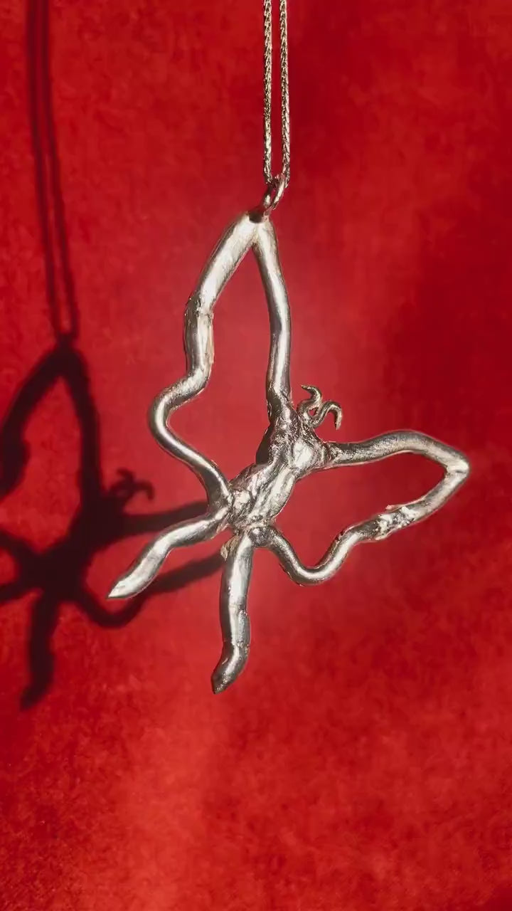 Silver Butterfly Charm dangling on a silver necklace rotating in front of a red velvet background.