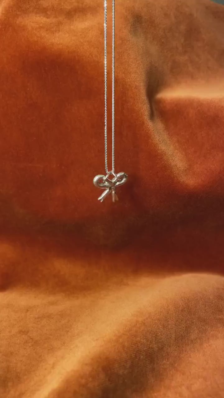 Silver ribbon charm on a silver necklace dangling on an orange background. 
