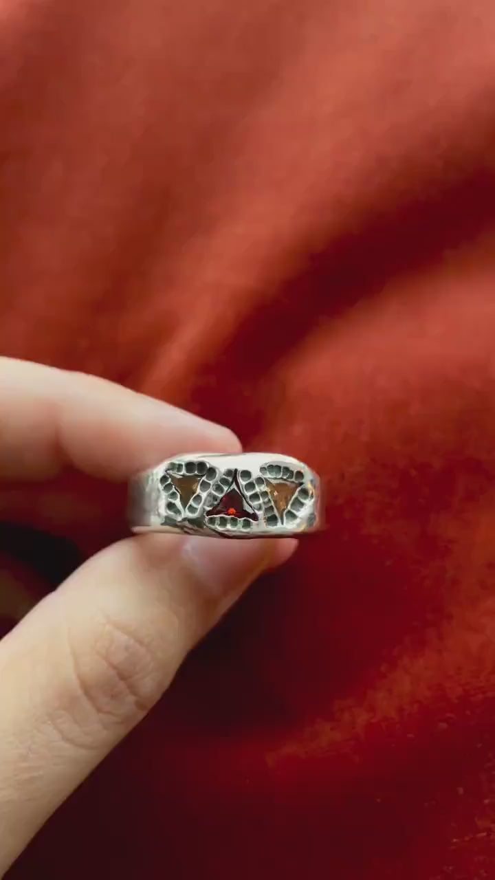 Top down video of a model's hand holding a silver ring with three stone set in the band of the ring. Two stones are yellow with one red stone, lining the top of the ring. 