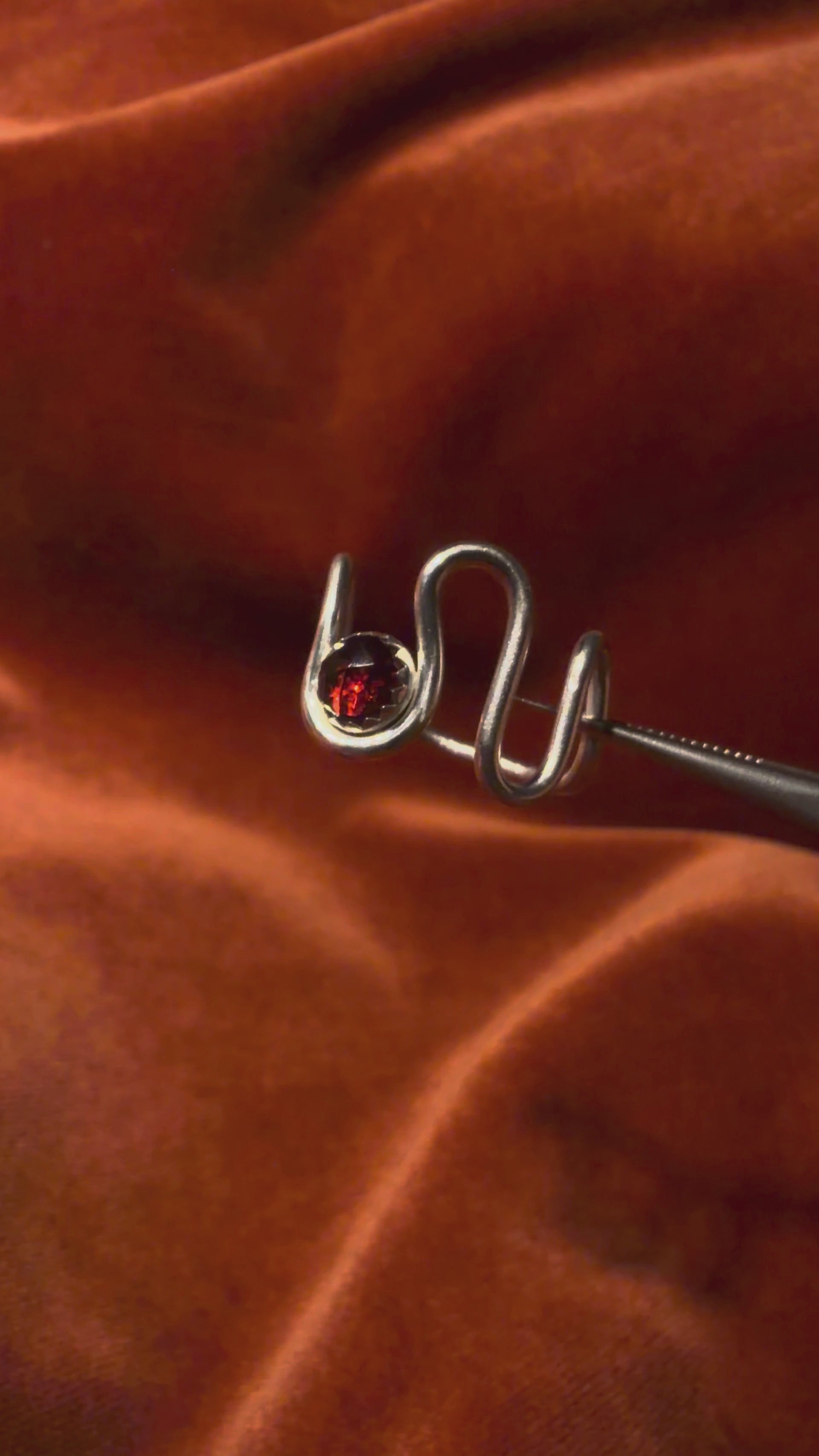 Video of silver ring with a asymmetrical band. A red rose cut garnet stone is set in a serrate bezel floating between the wavy band. 