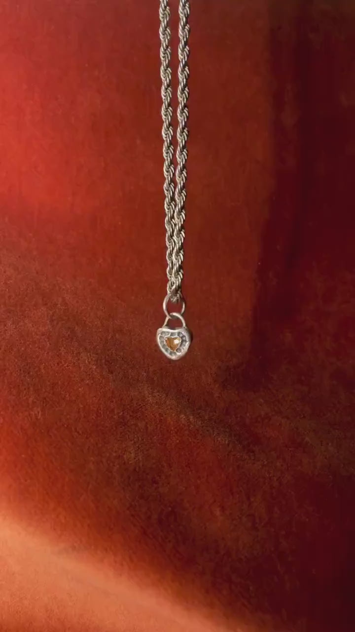 Small silver heart shaped charm with a small stone set in the center dangling from a silver chain.