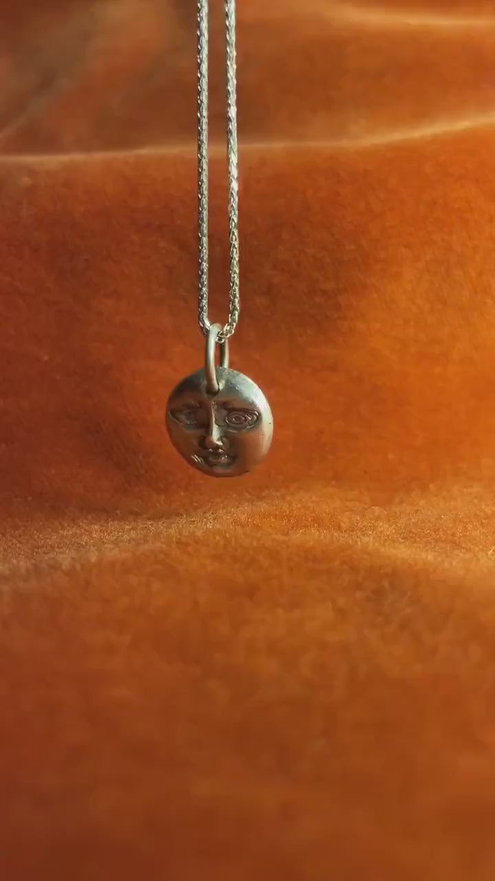 Silver moon charm with a face etched into it on a silver necklace.