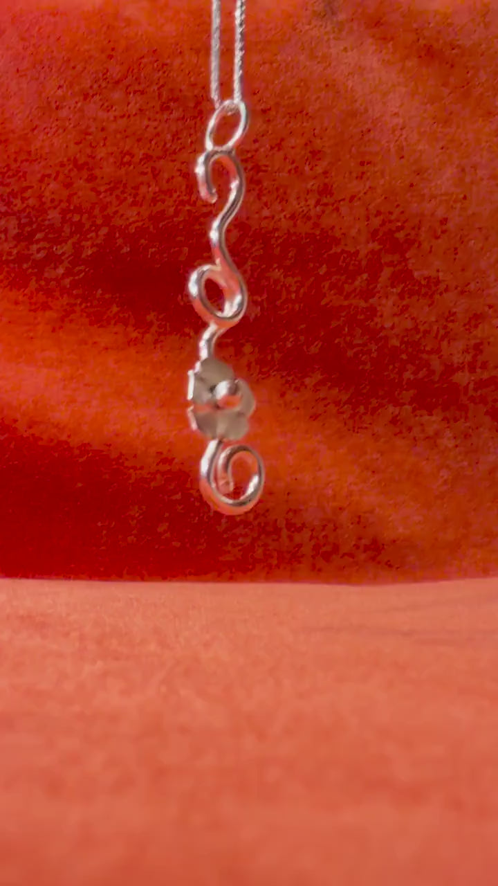 Video of a silver chain with a silver flower vine charm laying against an orange velvet background.