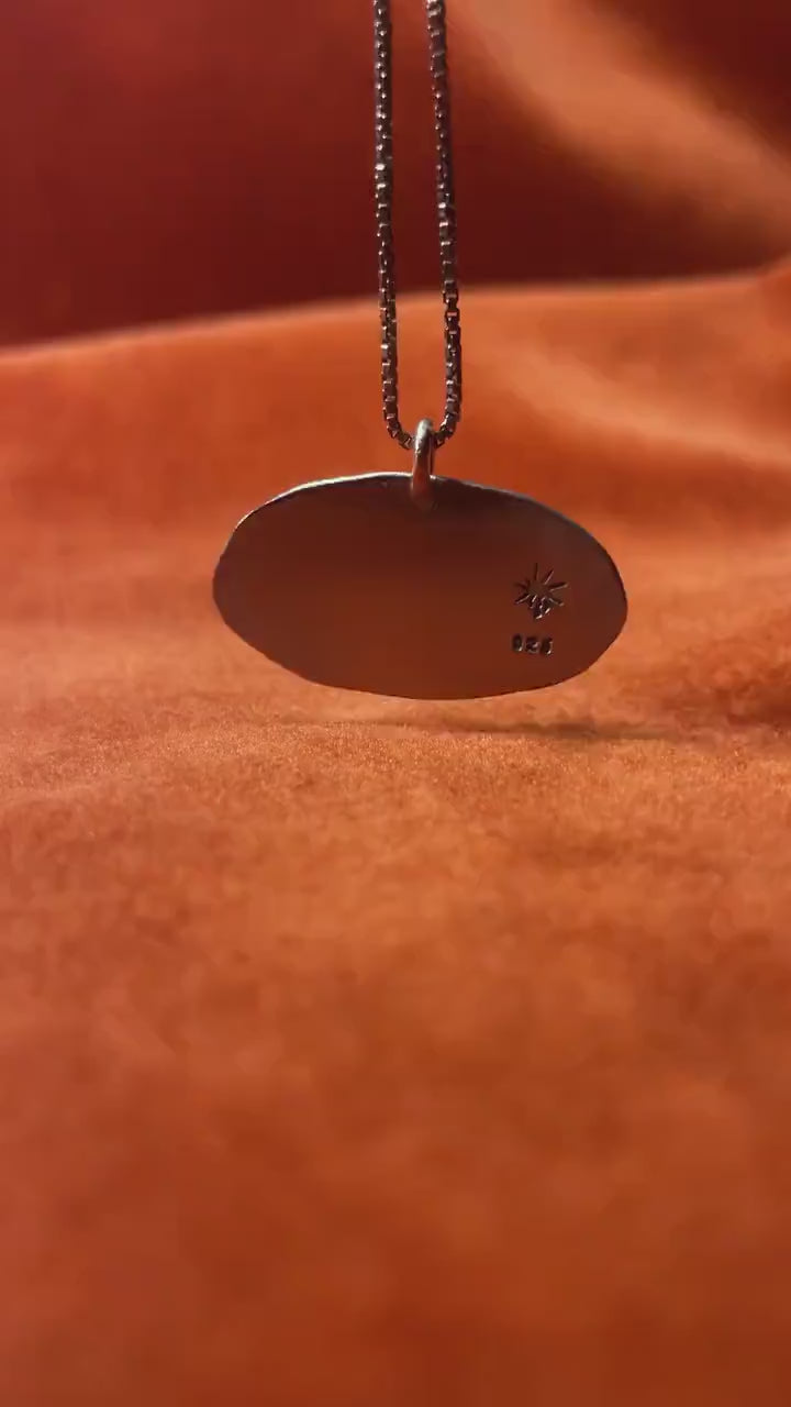 Silver swan pendant dandling from necklace on orange background.
