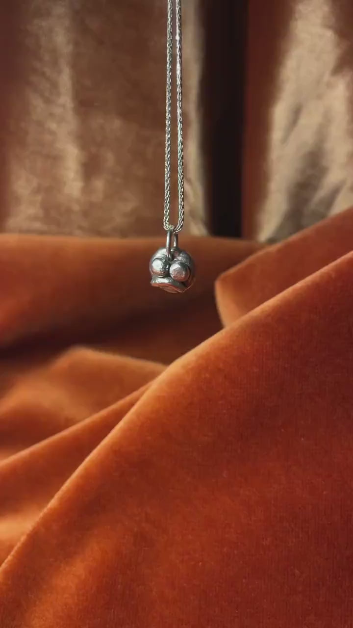 Silver frowning face charm on a silver necklace.