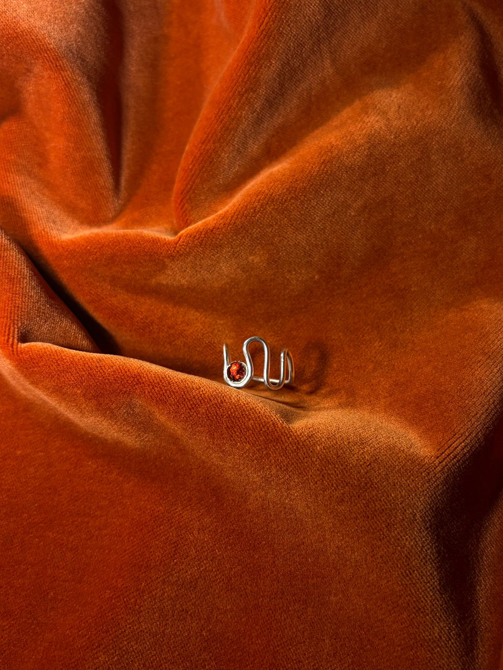 Silver ring with a asymmetrical band. A red rose cut garnet stone is set in a serrate bezel floating between the wavy band. 