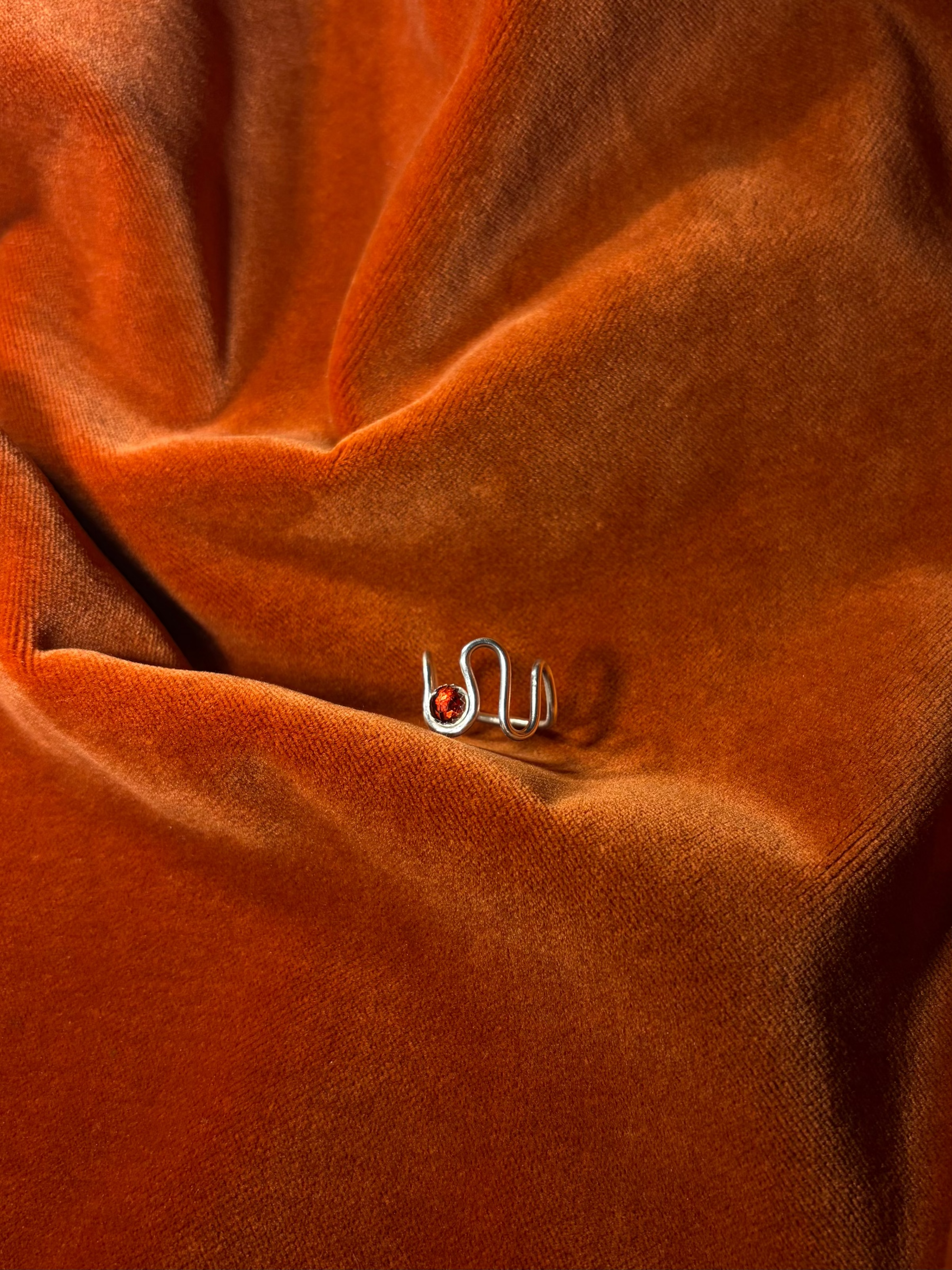 Silver ring with a asymmetrical band. A red rose cut garnet stone is set in a serrate bezel floating between the wavy band. 