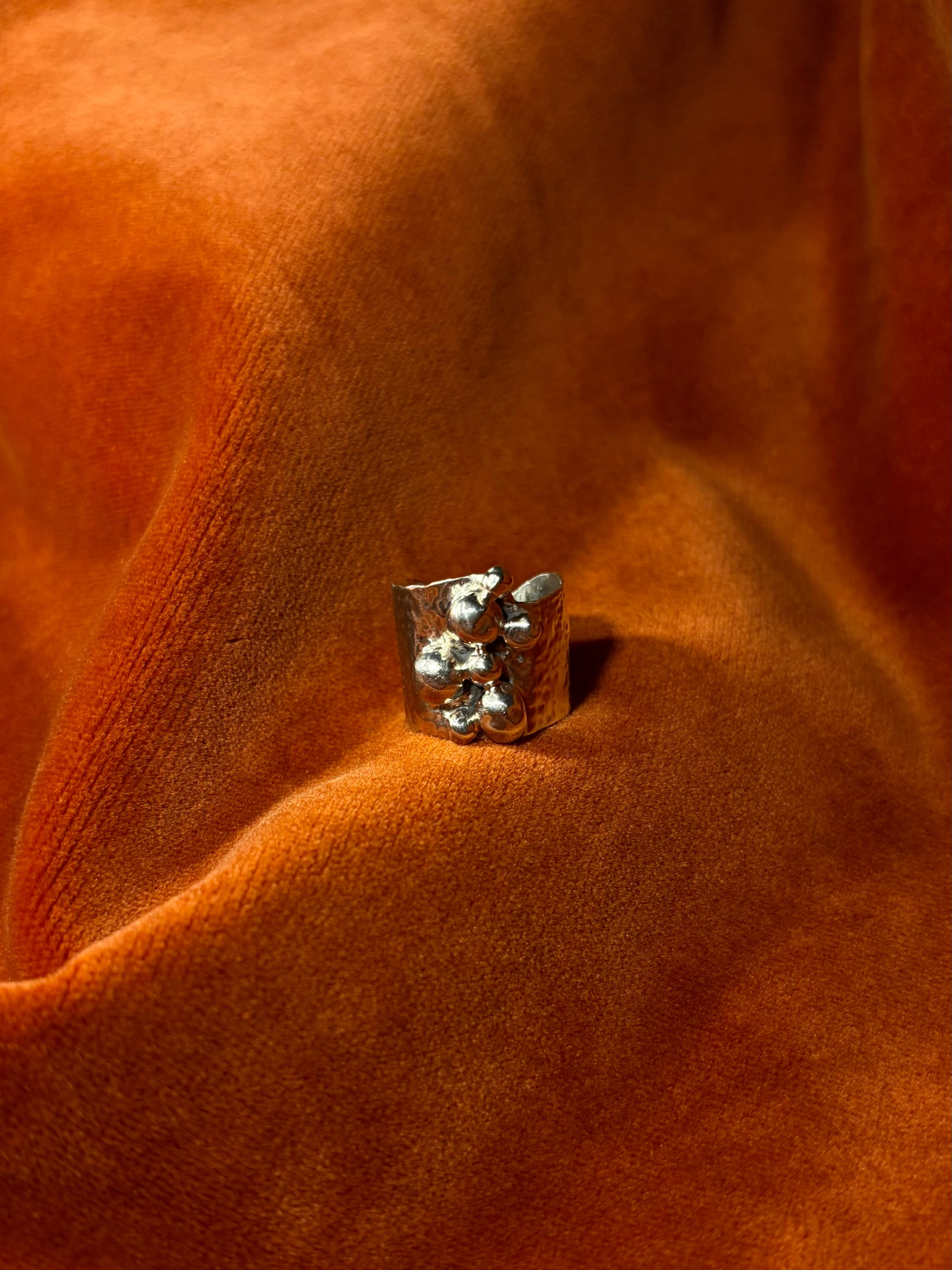 Close up image of a silver ring with a chunky hammered texture band. Seven varying sizes of orbs sit asymmetrically on top of the band.
