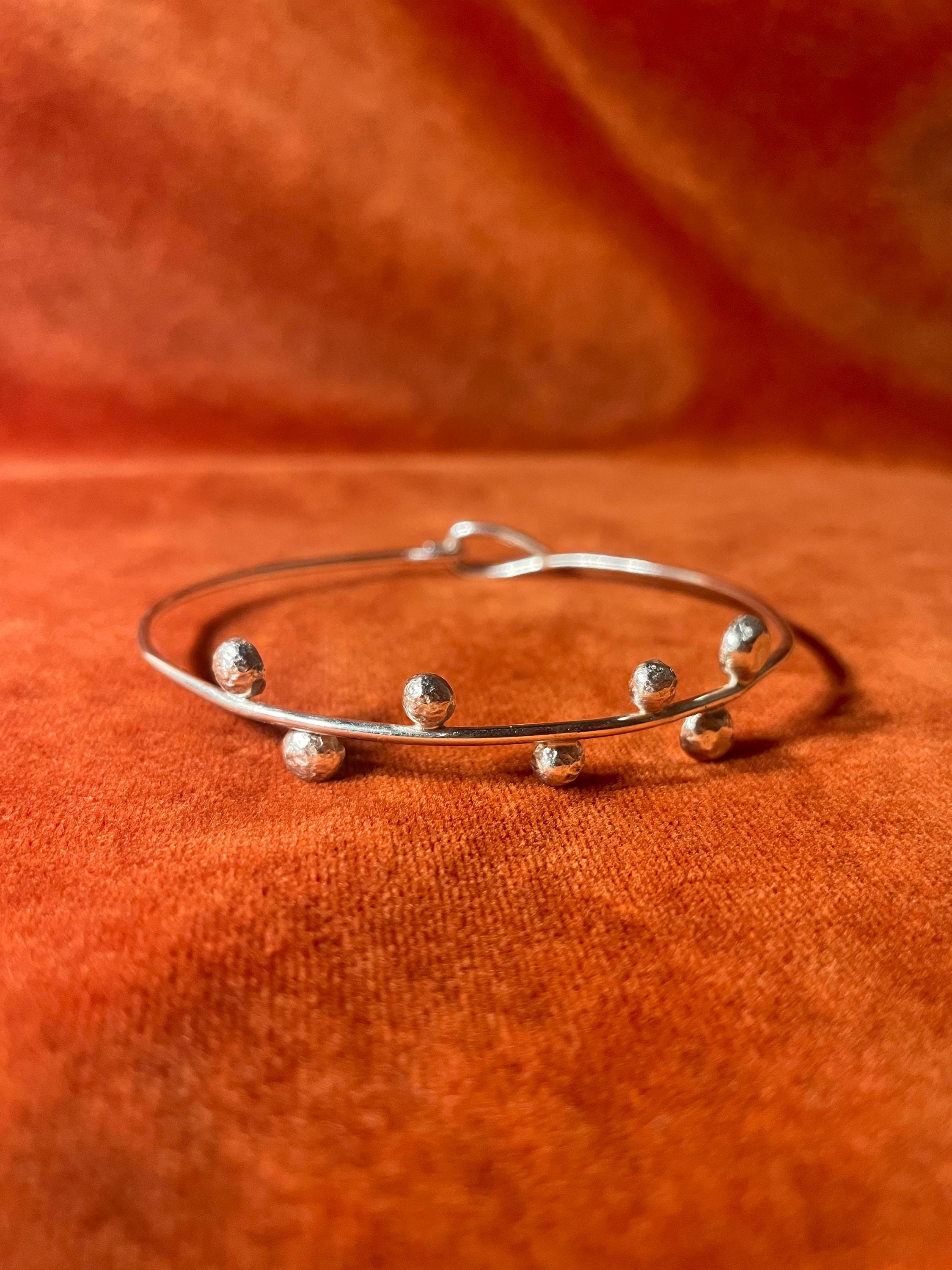 Front view of a silver bracelet with seven small orbs on the front and a closed hook clasp. Stage on an orange velvet background.